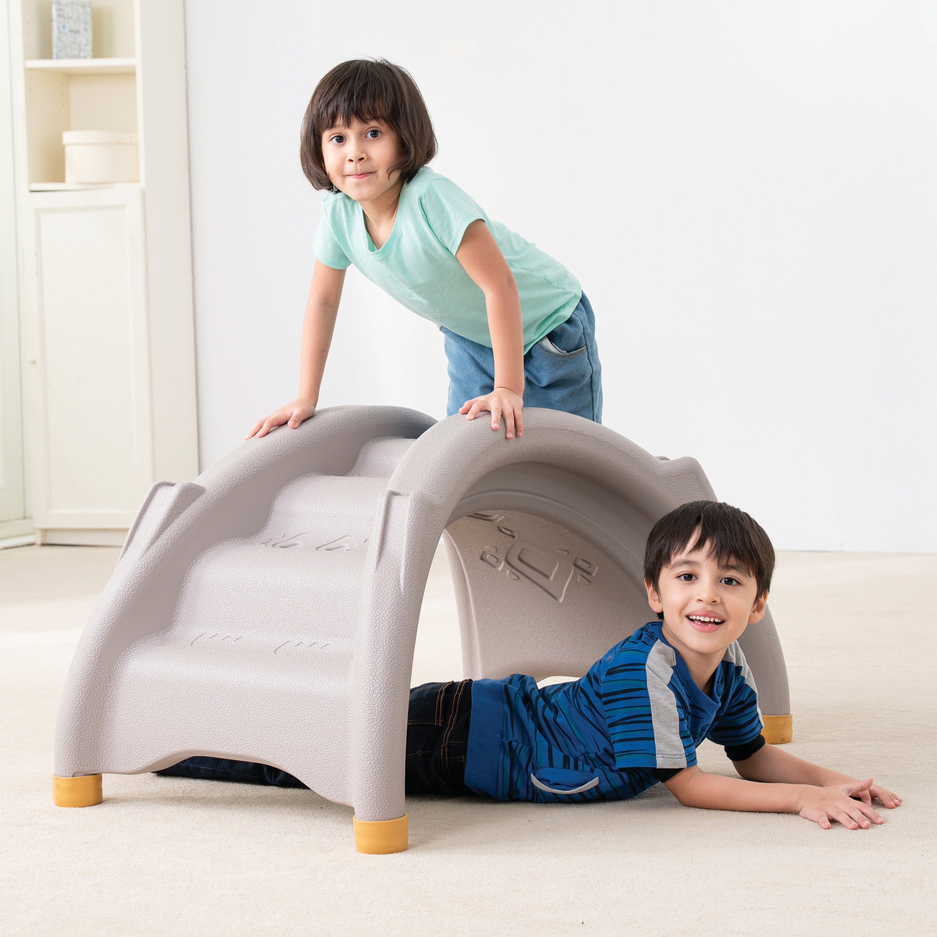 Two children playing with a plastic play structure indoors.
