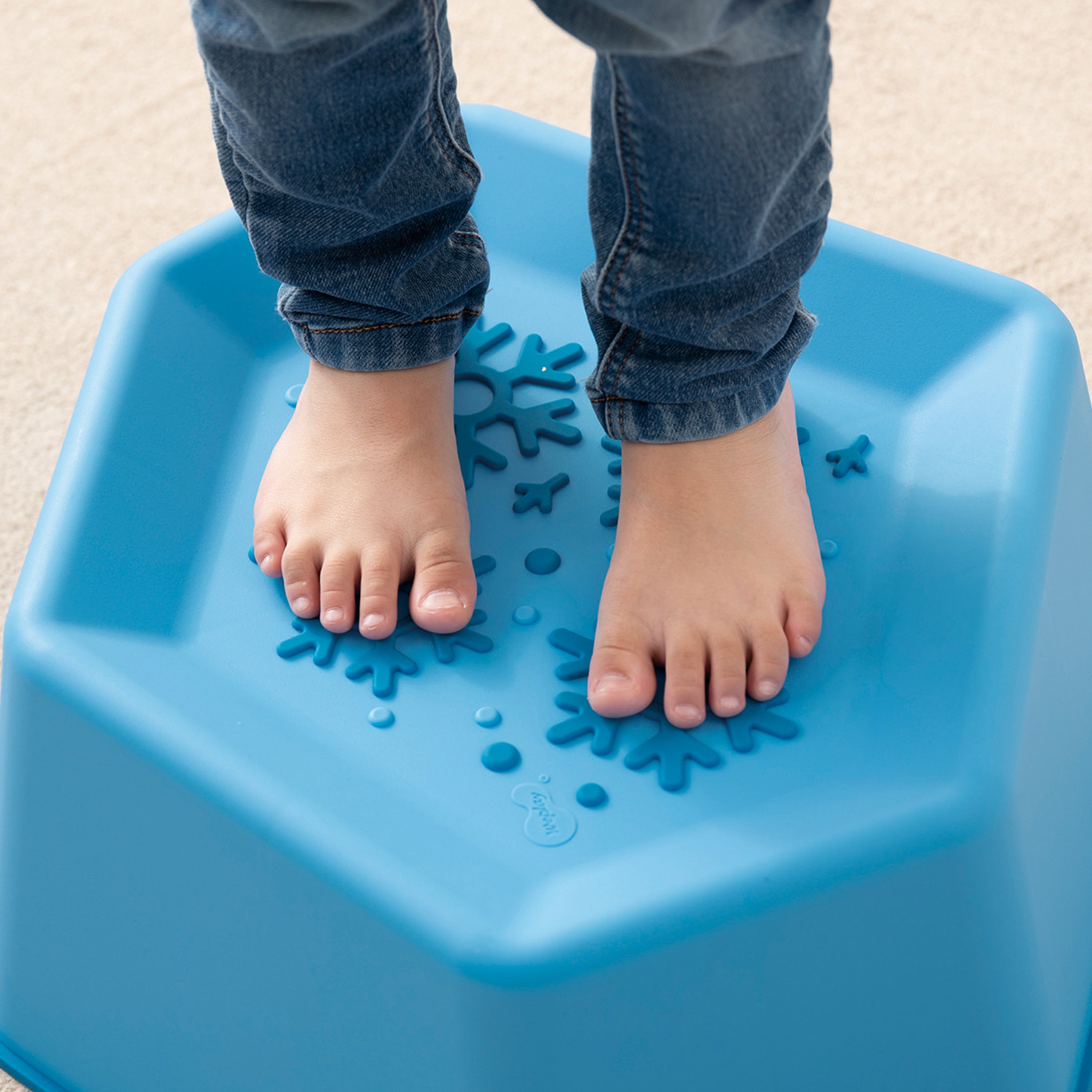 Child's feet standing on a blue step stool with textured surface