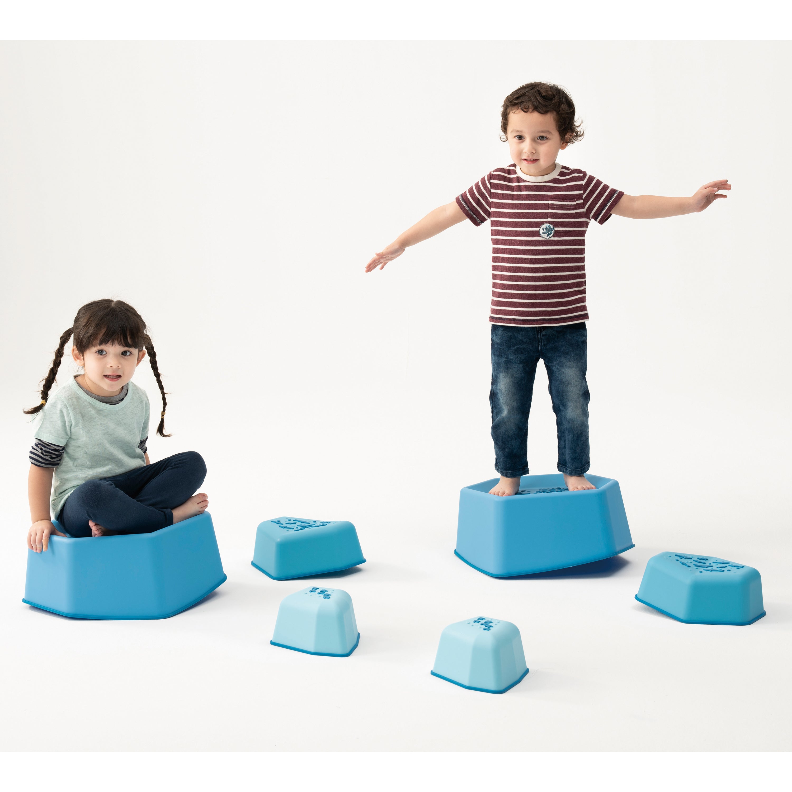 Two children playing with blue foam steps on a white background