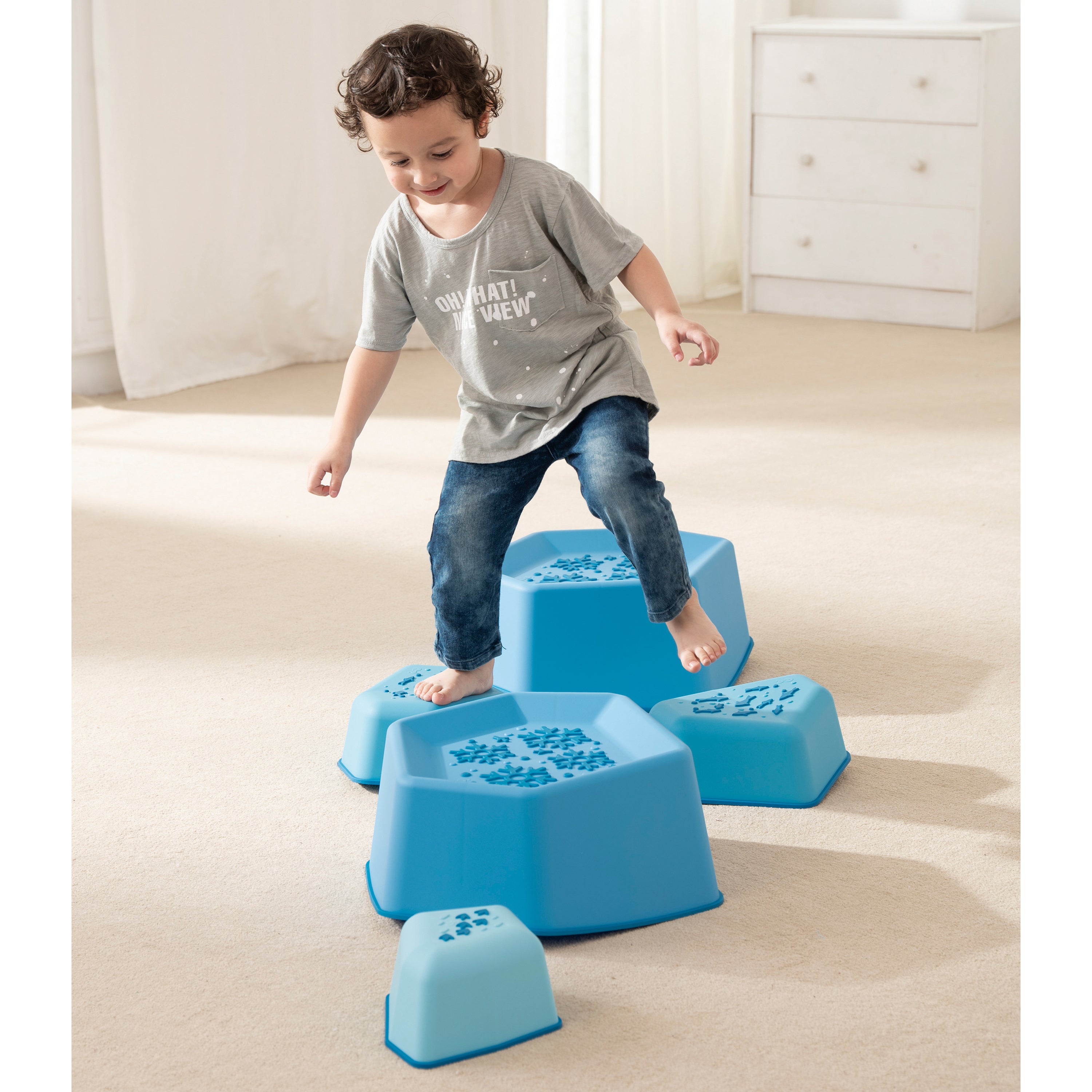 Child playing with blue step stools on a carpeted floor.