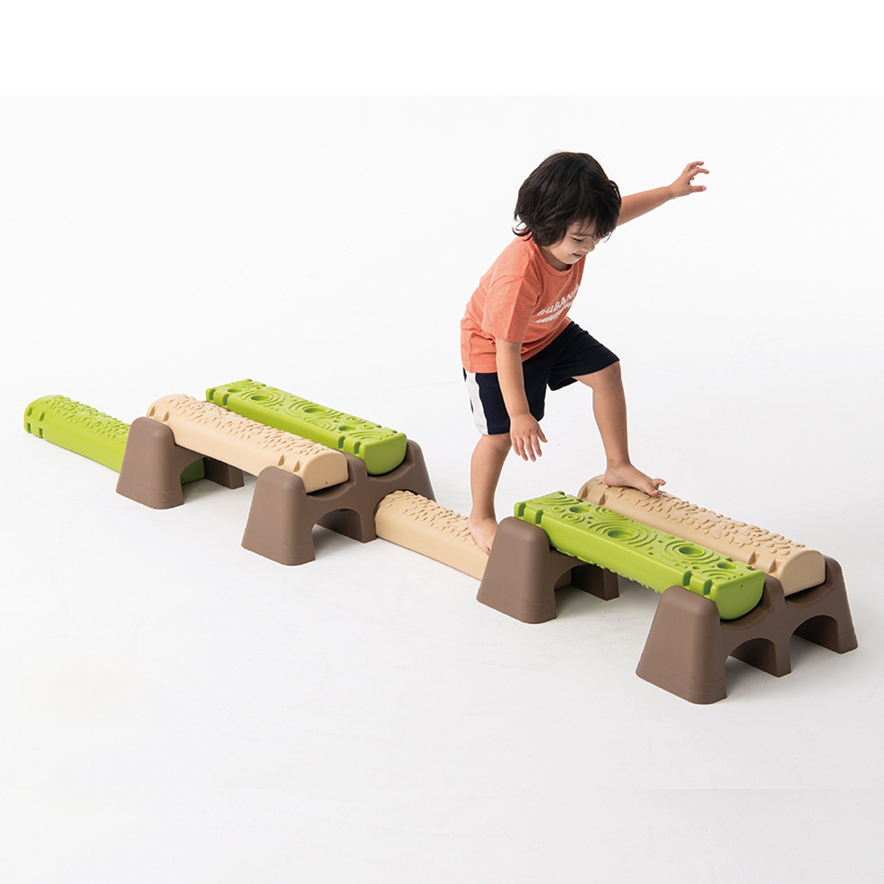 Child playing on a set of plastic balance beams with green and brown colors on a white background