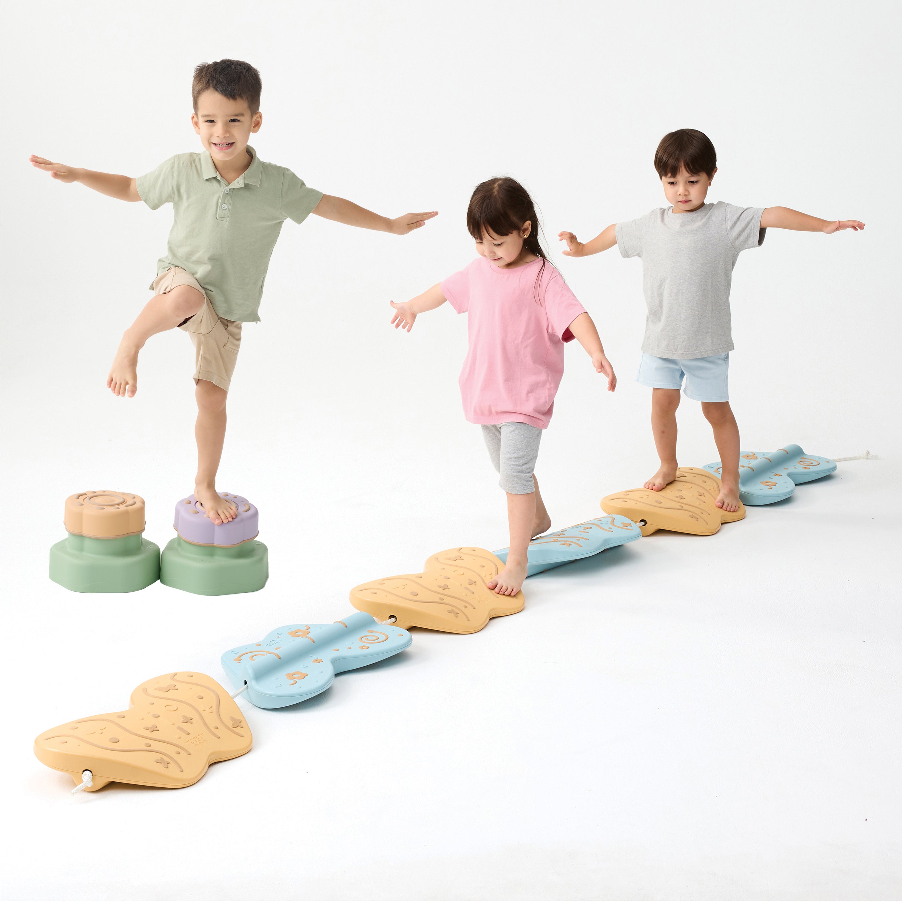 Three children balancing on colorful stepping stones on a white background