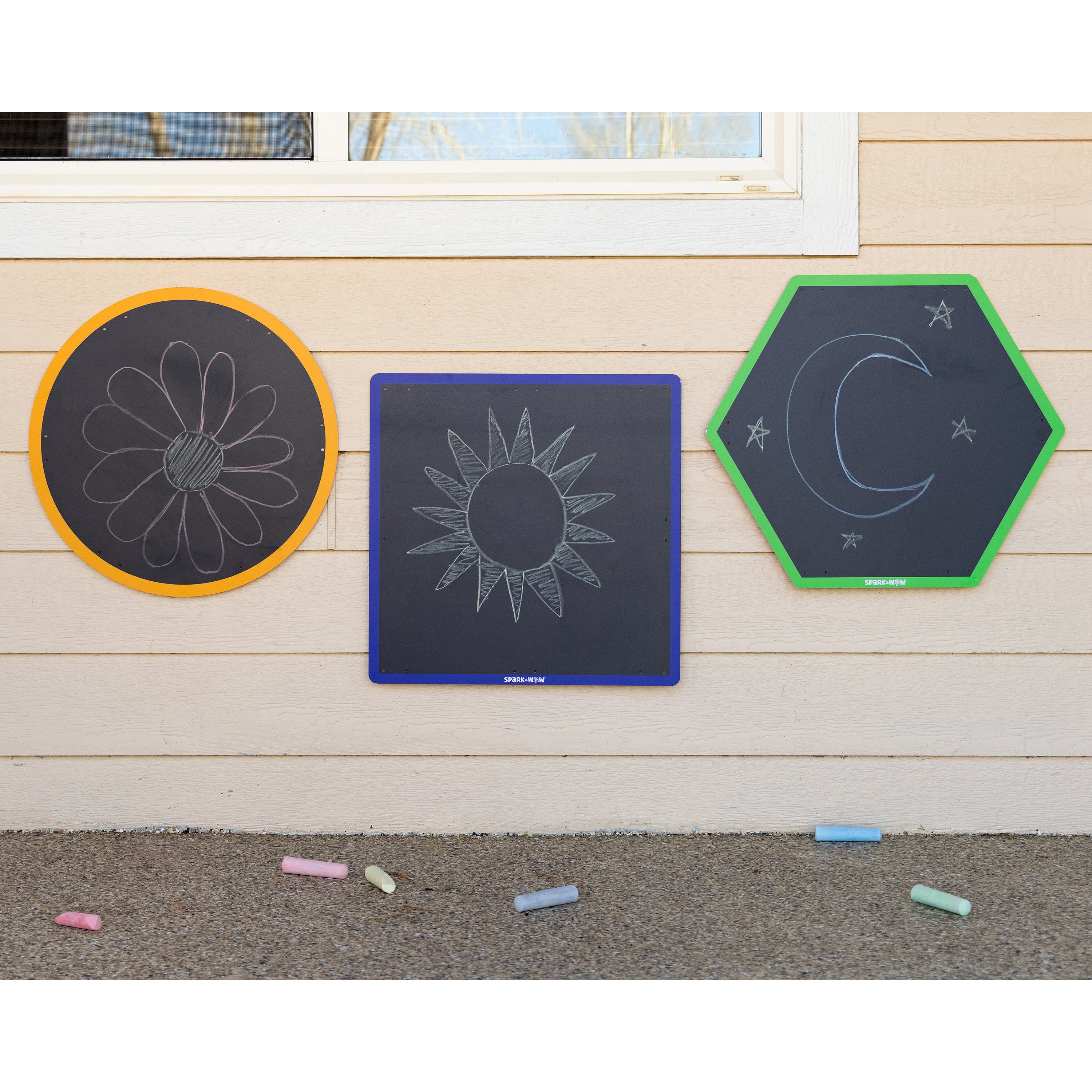 Three hexagonal chalkboards with different designs on a wooden surface, with colorful chalks on the ground.