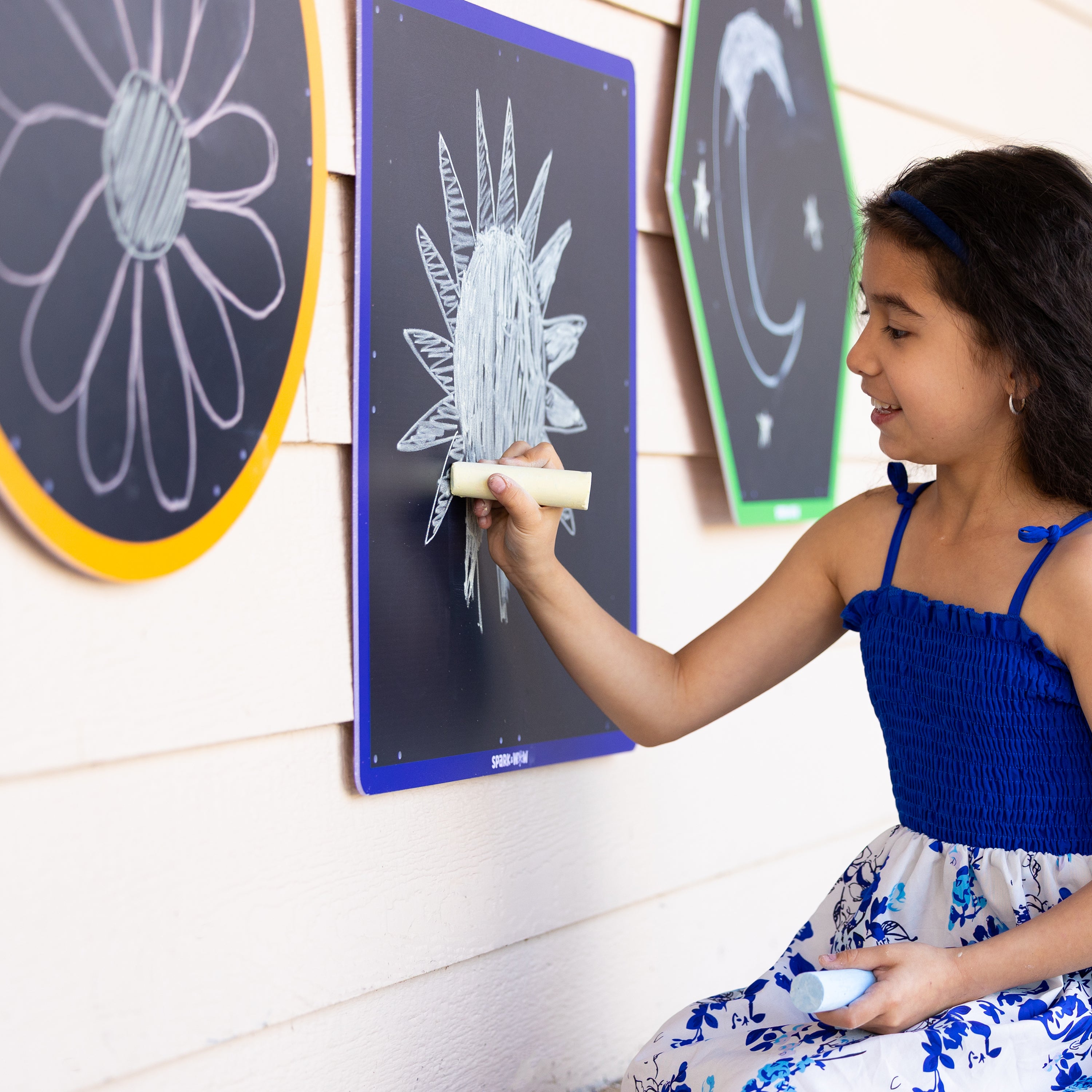 Young girl drawing on a chalkboard wall with colorful chalk.
