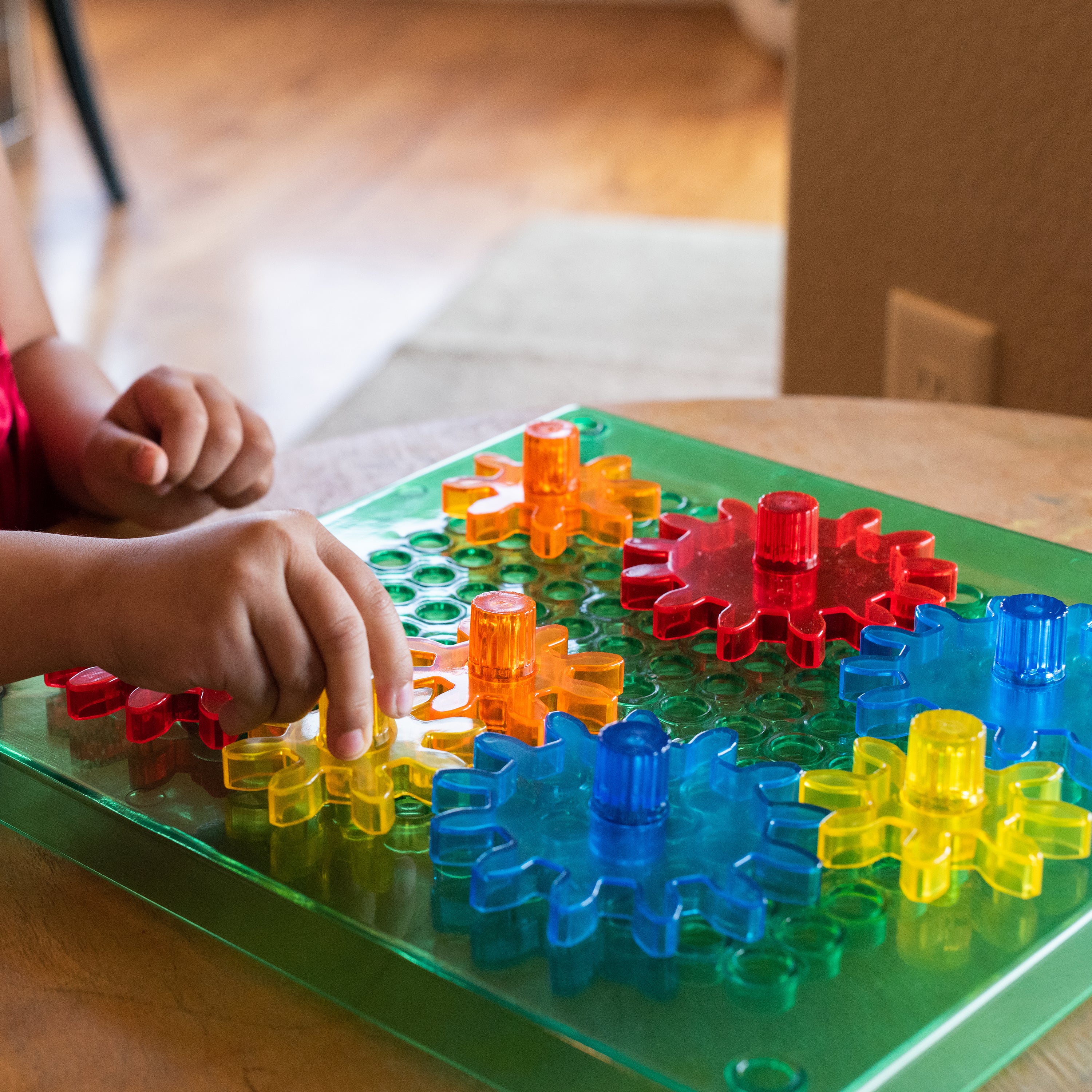 Children playing with colorful plastic gears on a green board.