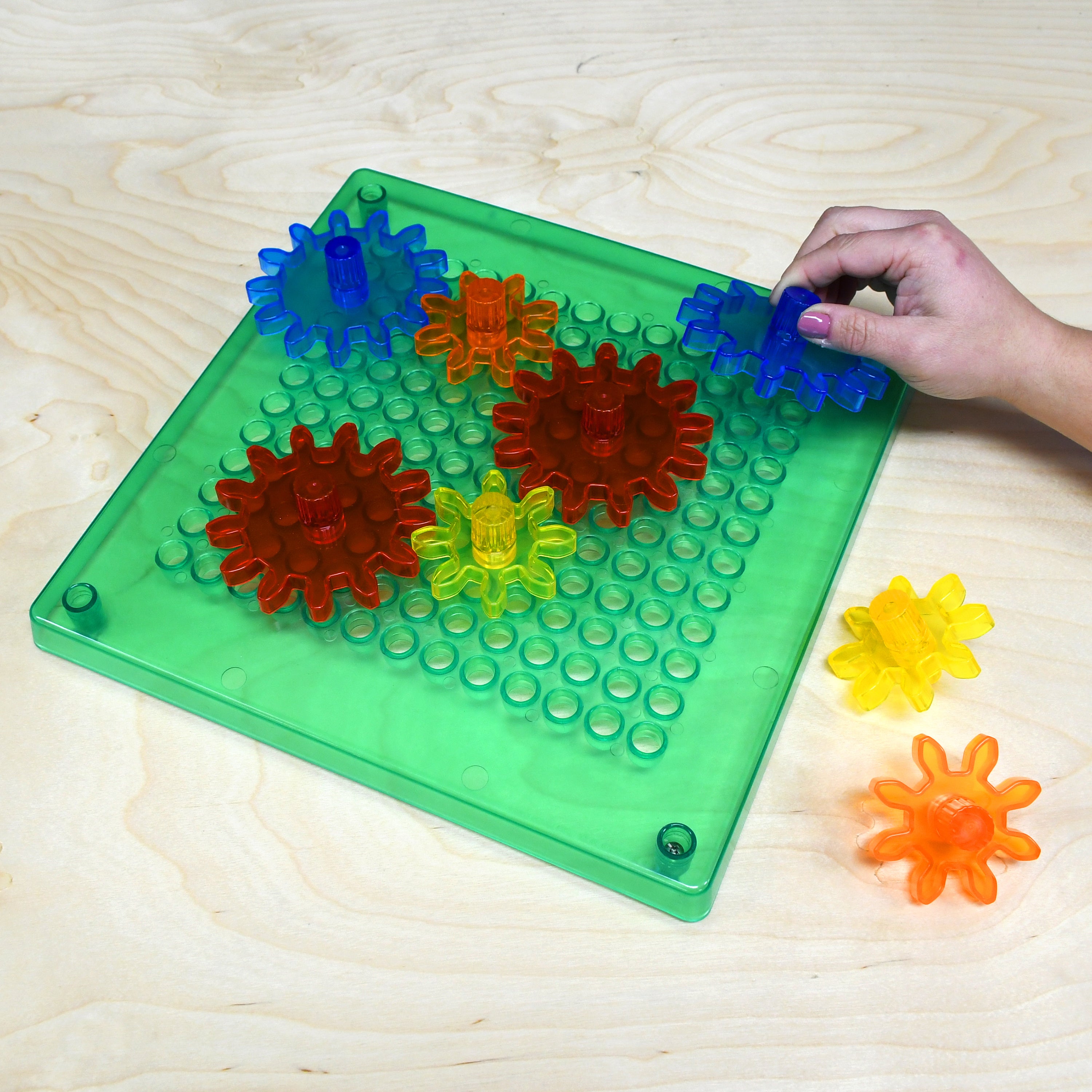 Colorful gear-like toys on a green baseplate with a hand interacting with them on a wooden surface.