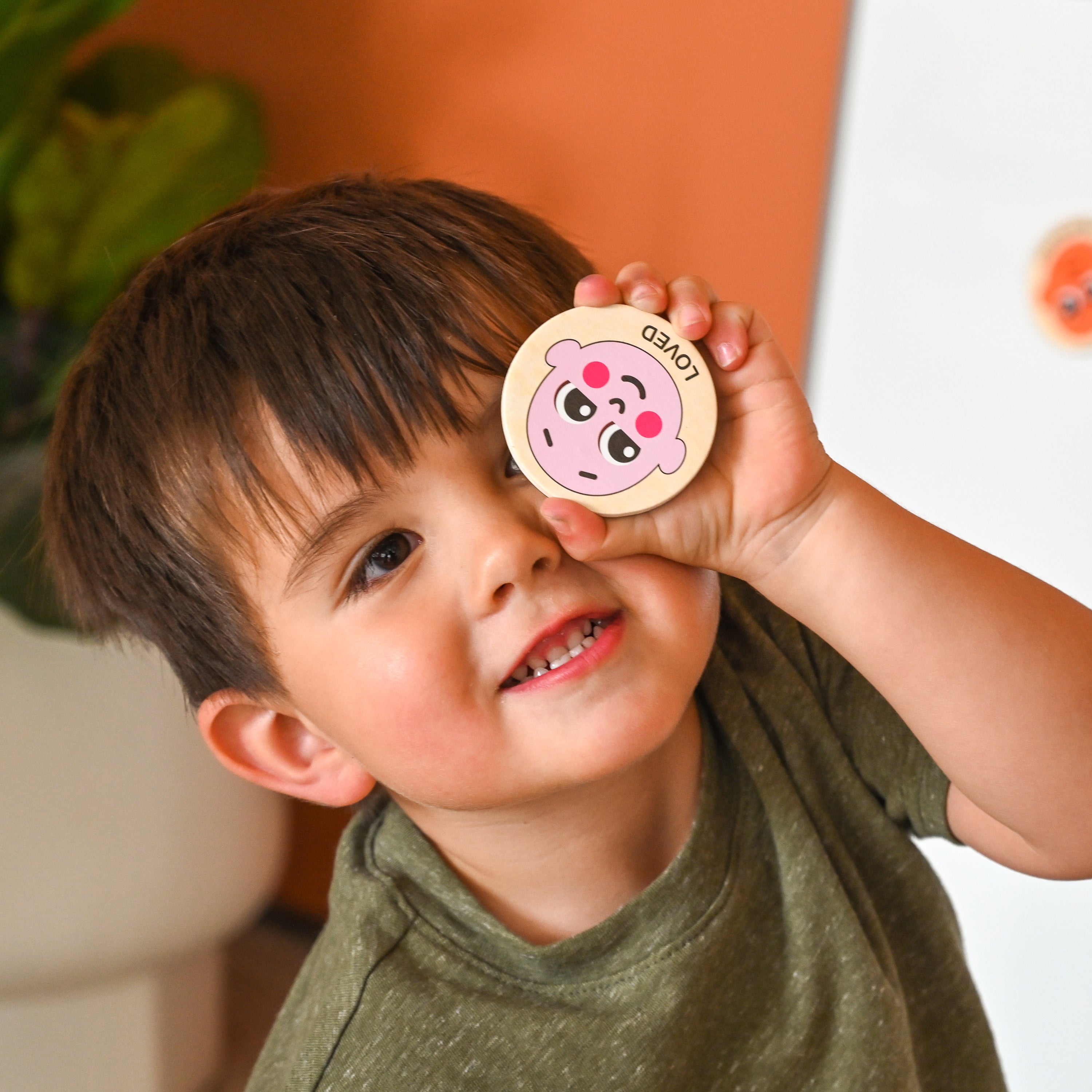 Child showcasing a button with a face and the word loved engraved on it