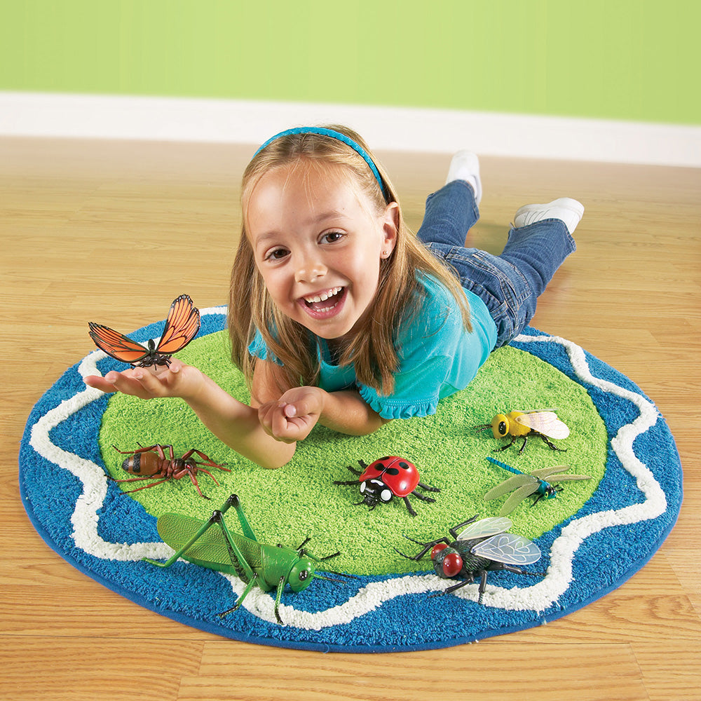 Child playing with toy insects on a rug shaped like a world map.