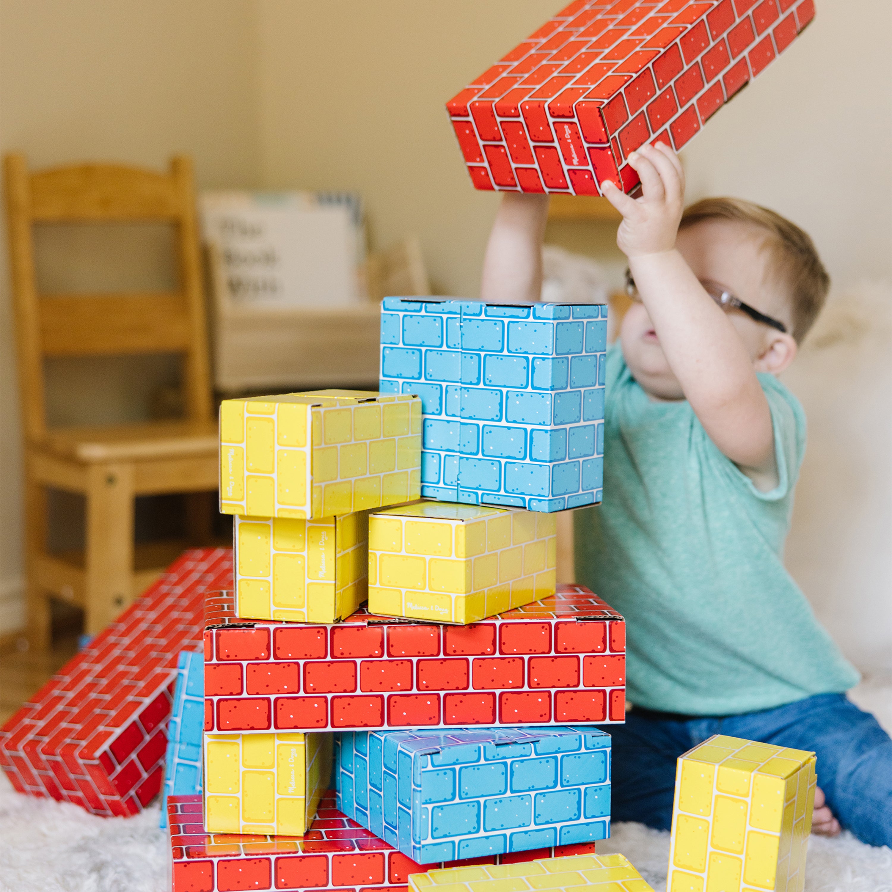 Child playing with colorful cardboard blocks in a room.
