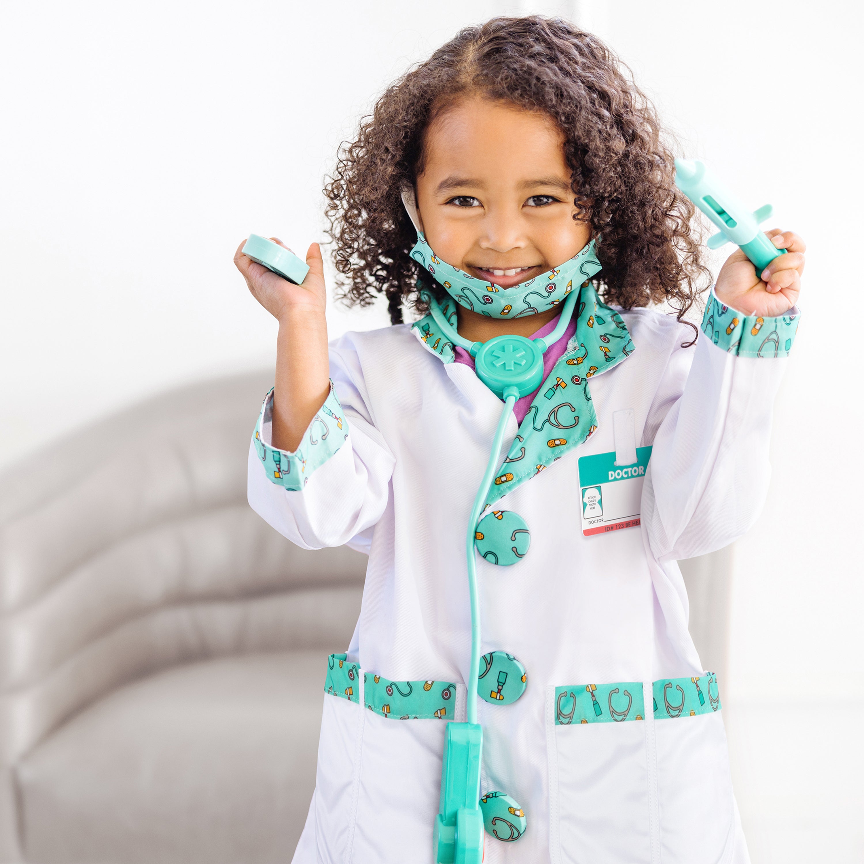 Child in a doctor's outfit with a stethoscope and toy medical tools on a white background