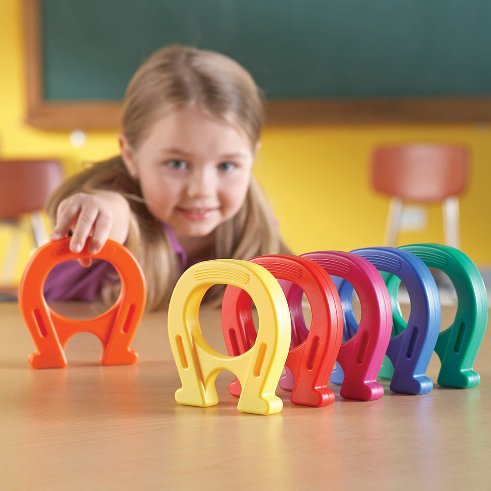 Colorful plastic horseshoe toys on a table with a child in a classroom setting.