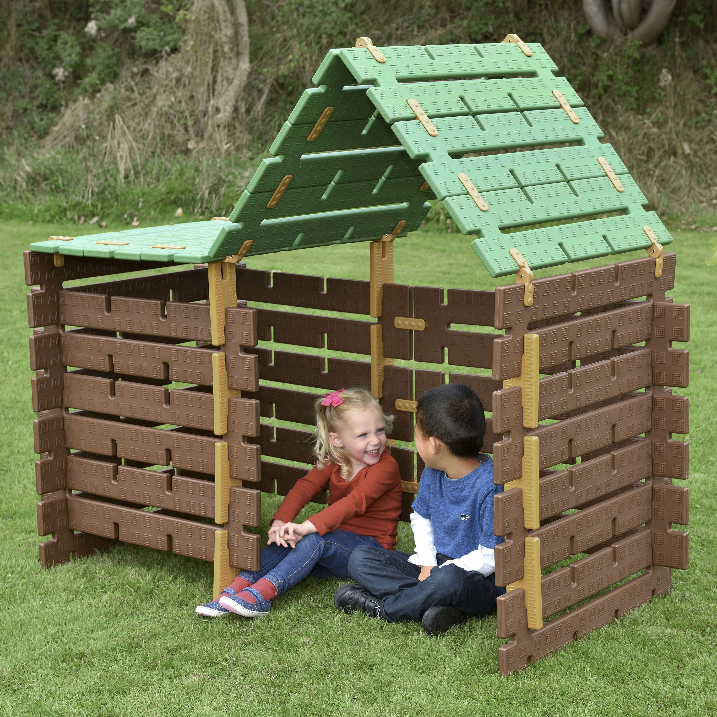 Children playing inside a plastic playhouse with green roof on grass