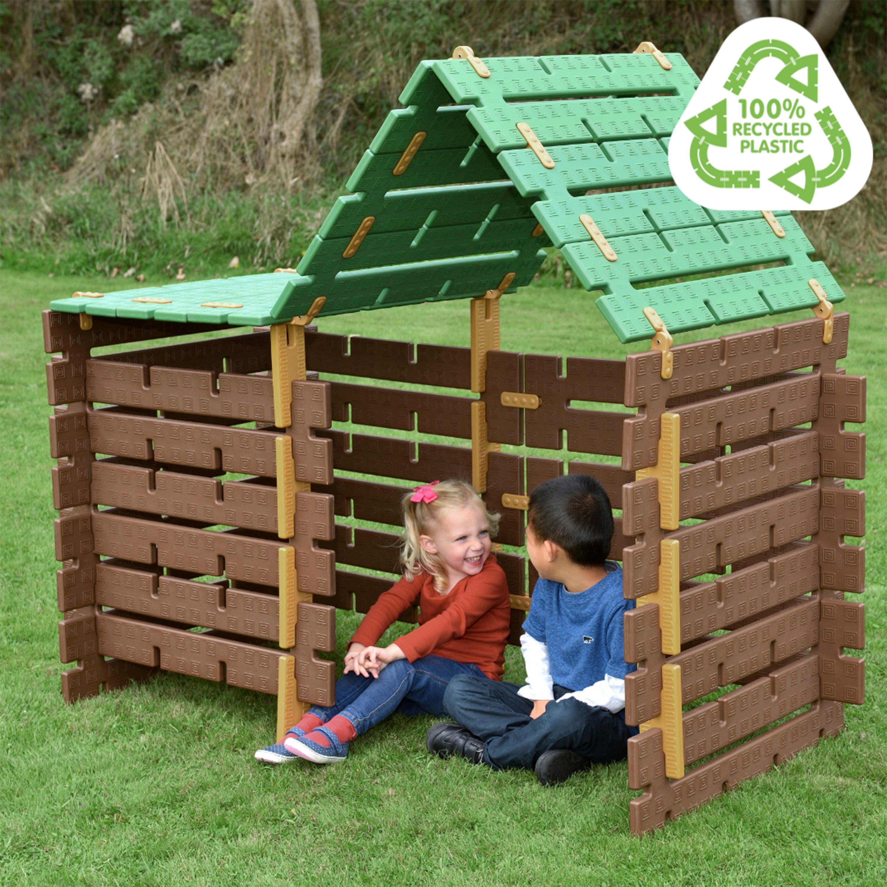 Children sitting on a recycled plastic playhouse with a green roof and '100% Recycled Plastic' label.