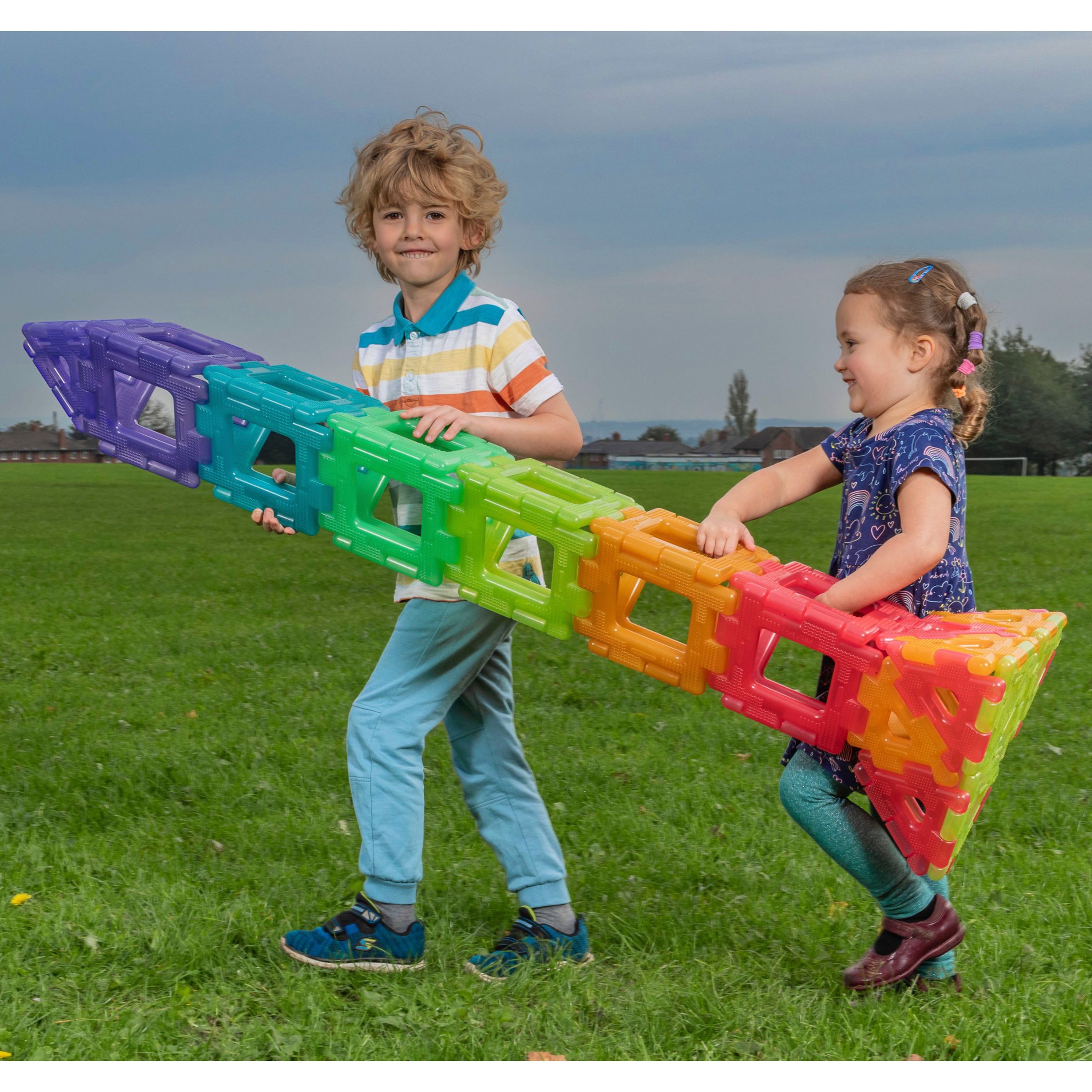 Two children playing with large colorful blocks on a grassy field.