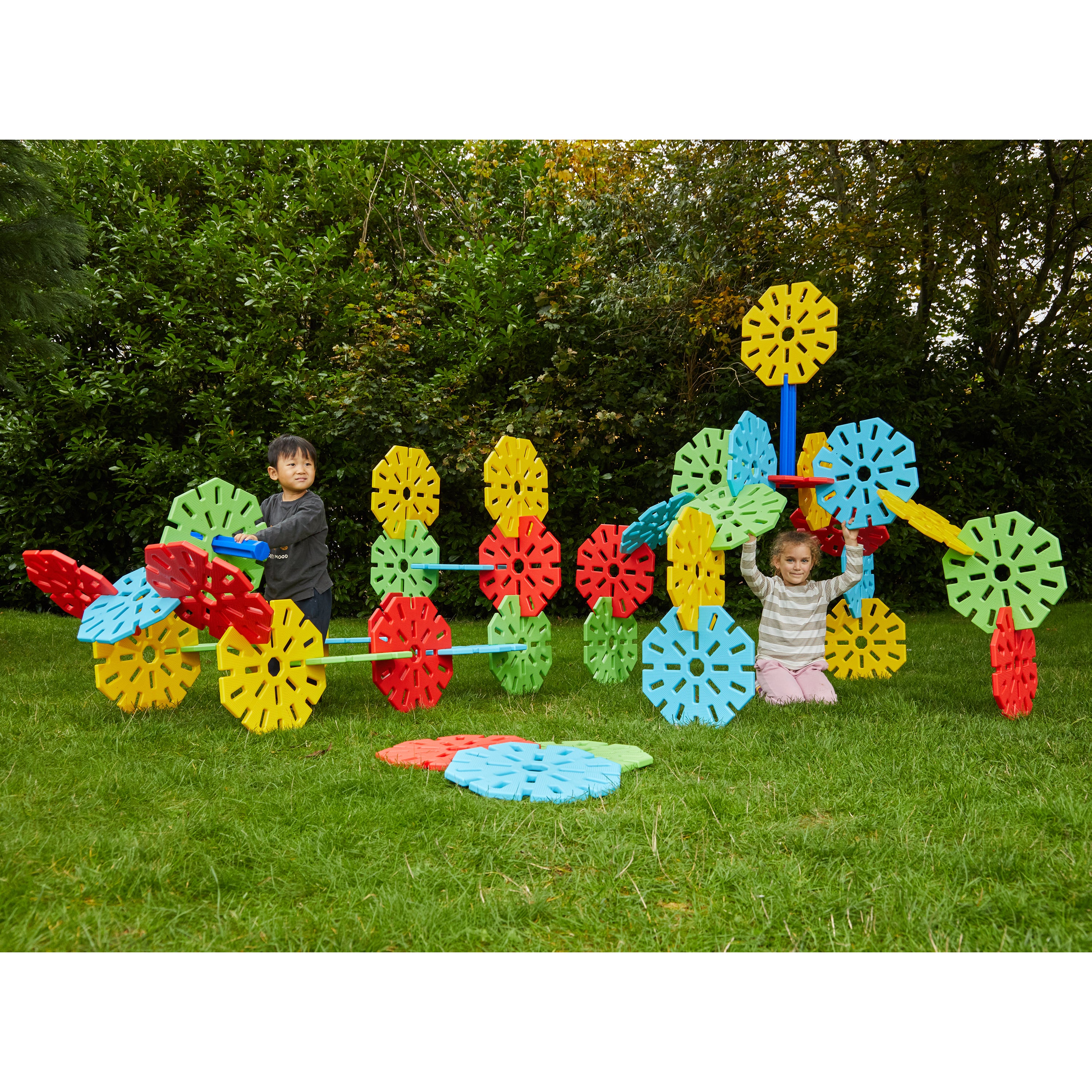 Children playing with a colorful outdoor play structure in a grassy area with trees in the background.
