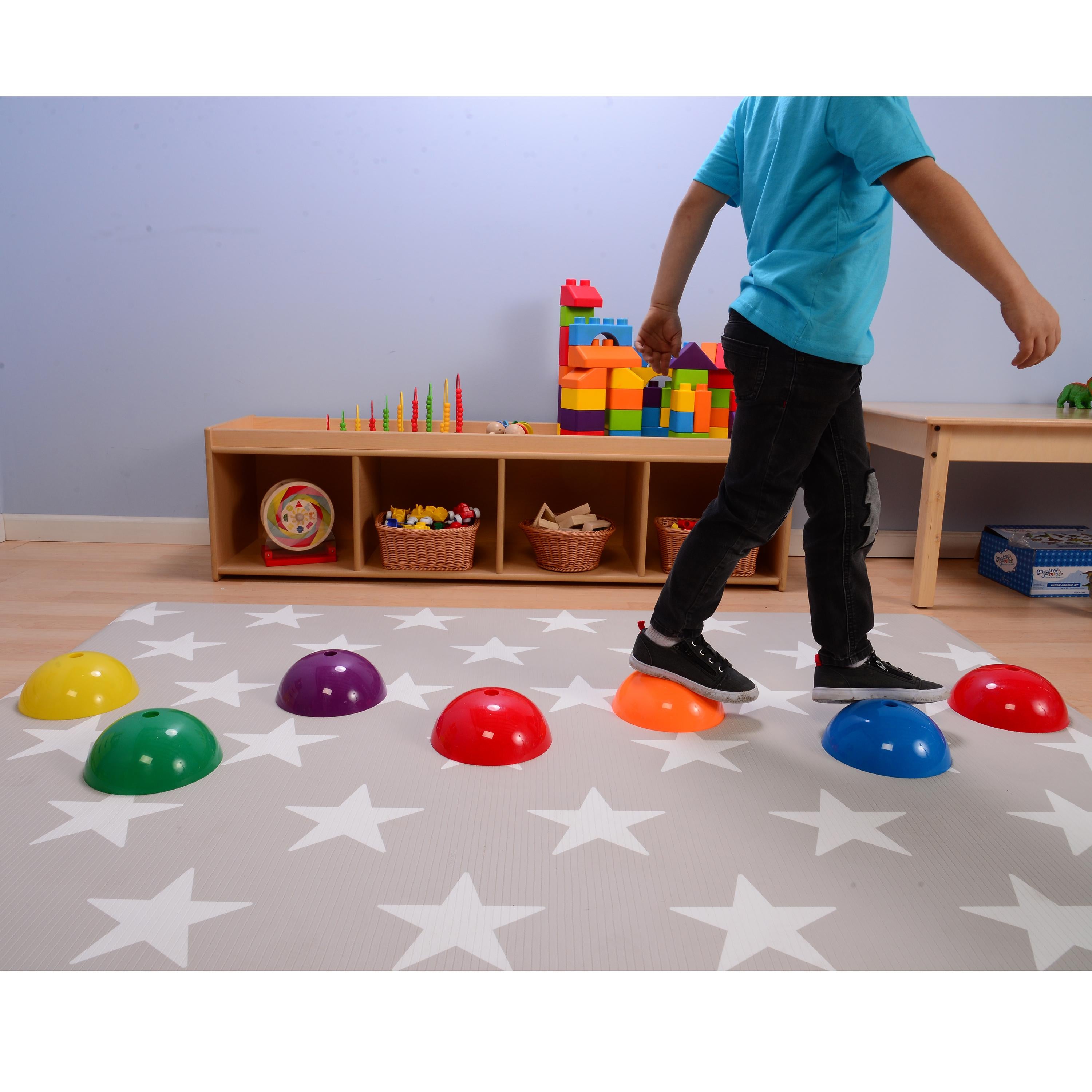 Child playing with colorful plastic stepping domes on a star-patterned mat in a room with toys and shelves.