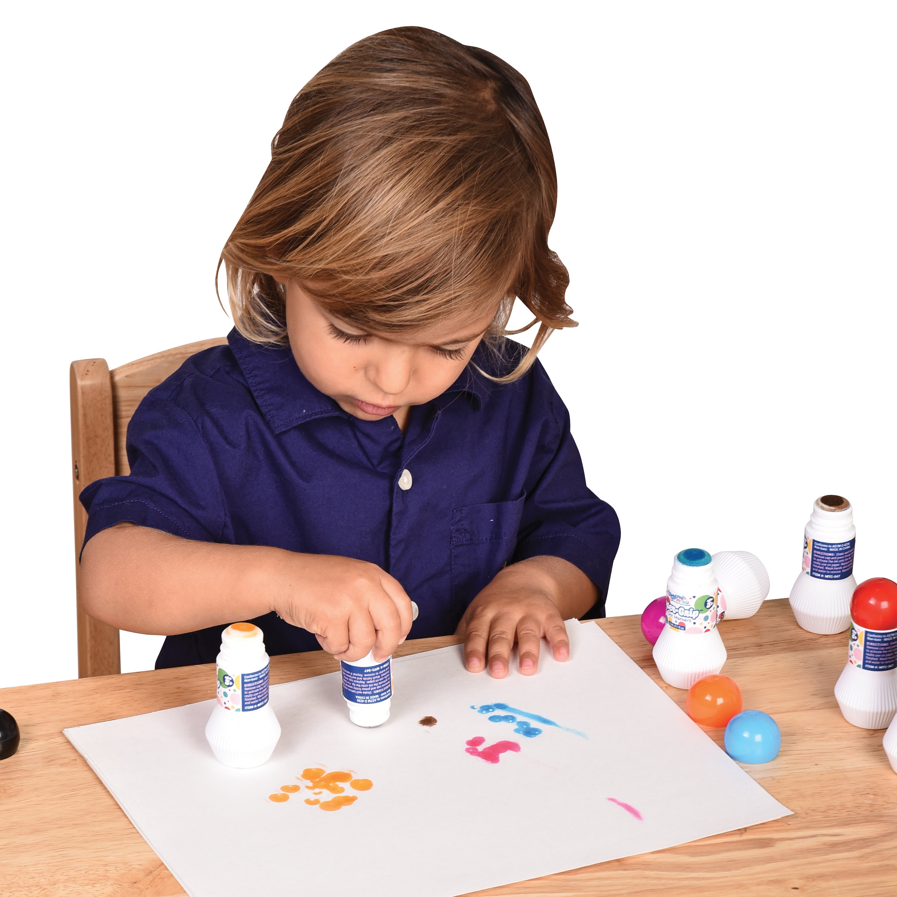 Child in a blue shirt playing with colorful bottles and paper at a table.
