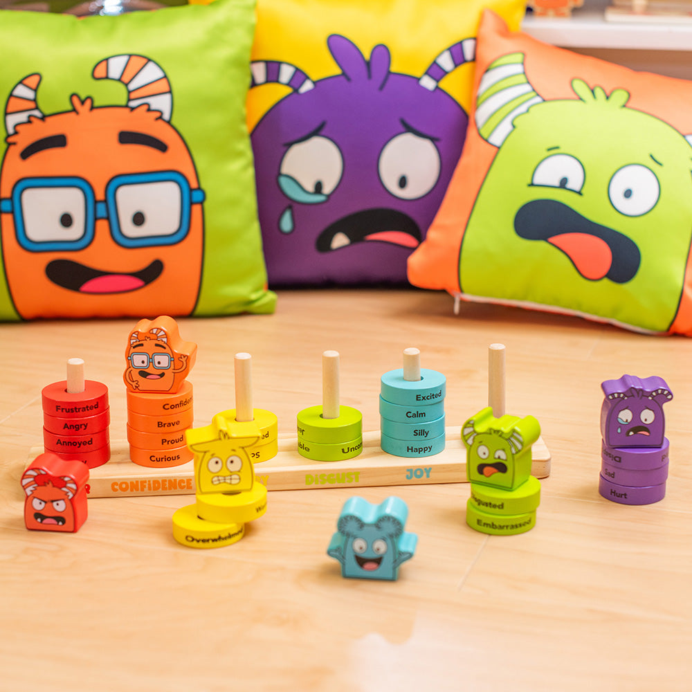 Colorful emotional expression toys on a wooden surface with character cushions in the background.