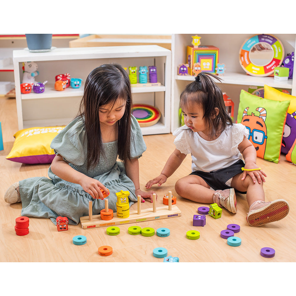 Two young girls playing with colorful educational toys on a wooden floor.
