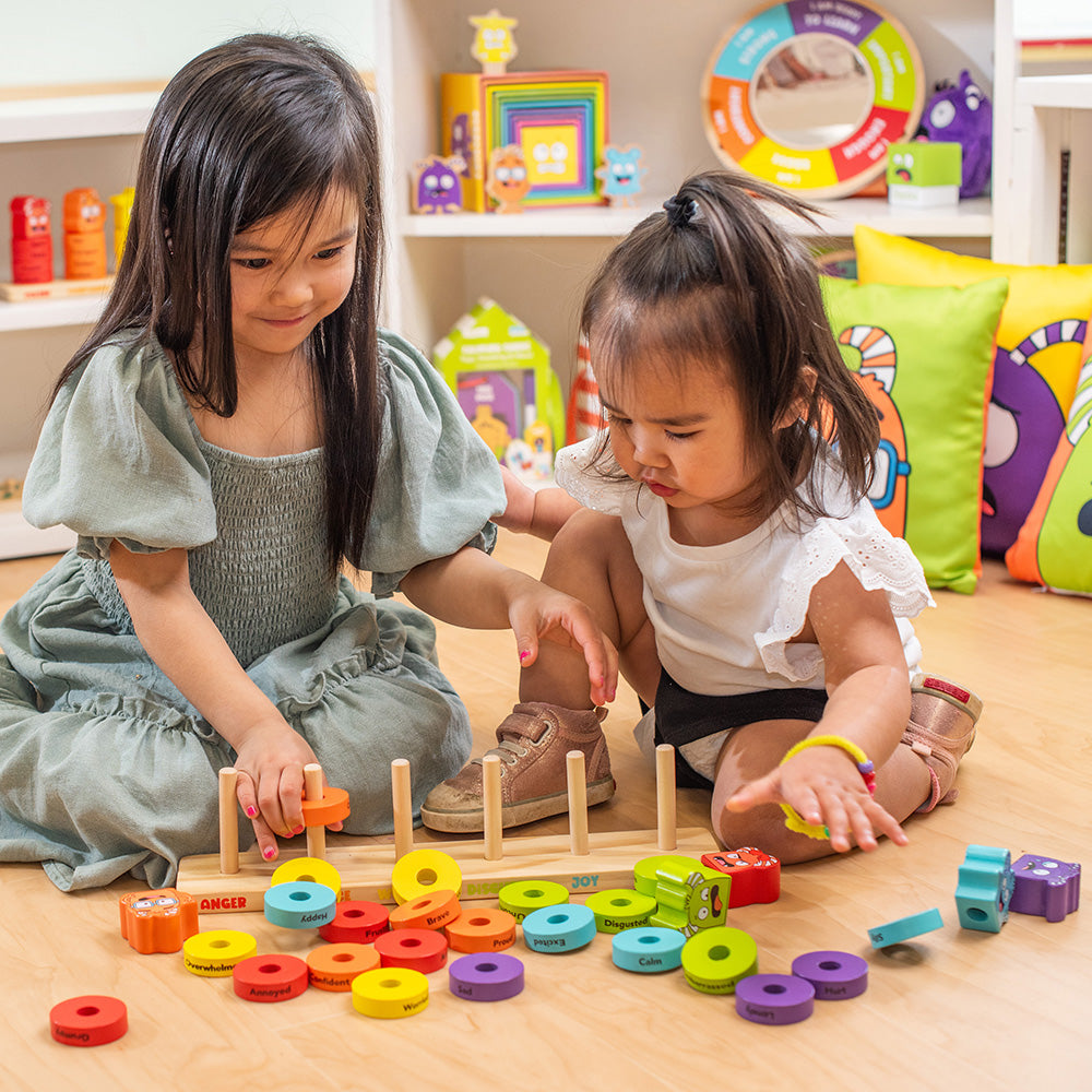 Two young girls playing with colorful educational toys on a wooden floor.