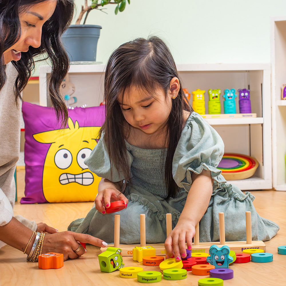 Woman and young girl playing with colorful educational toys on a wooden floor.