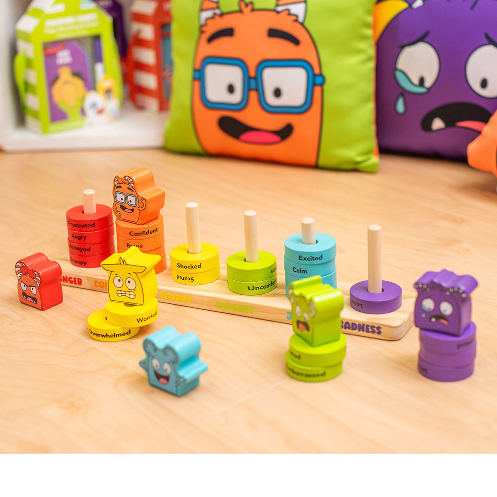 Colorful emotional expression toys on a wooden surface with cartoon character pillows in the background.