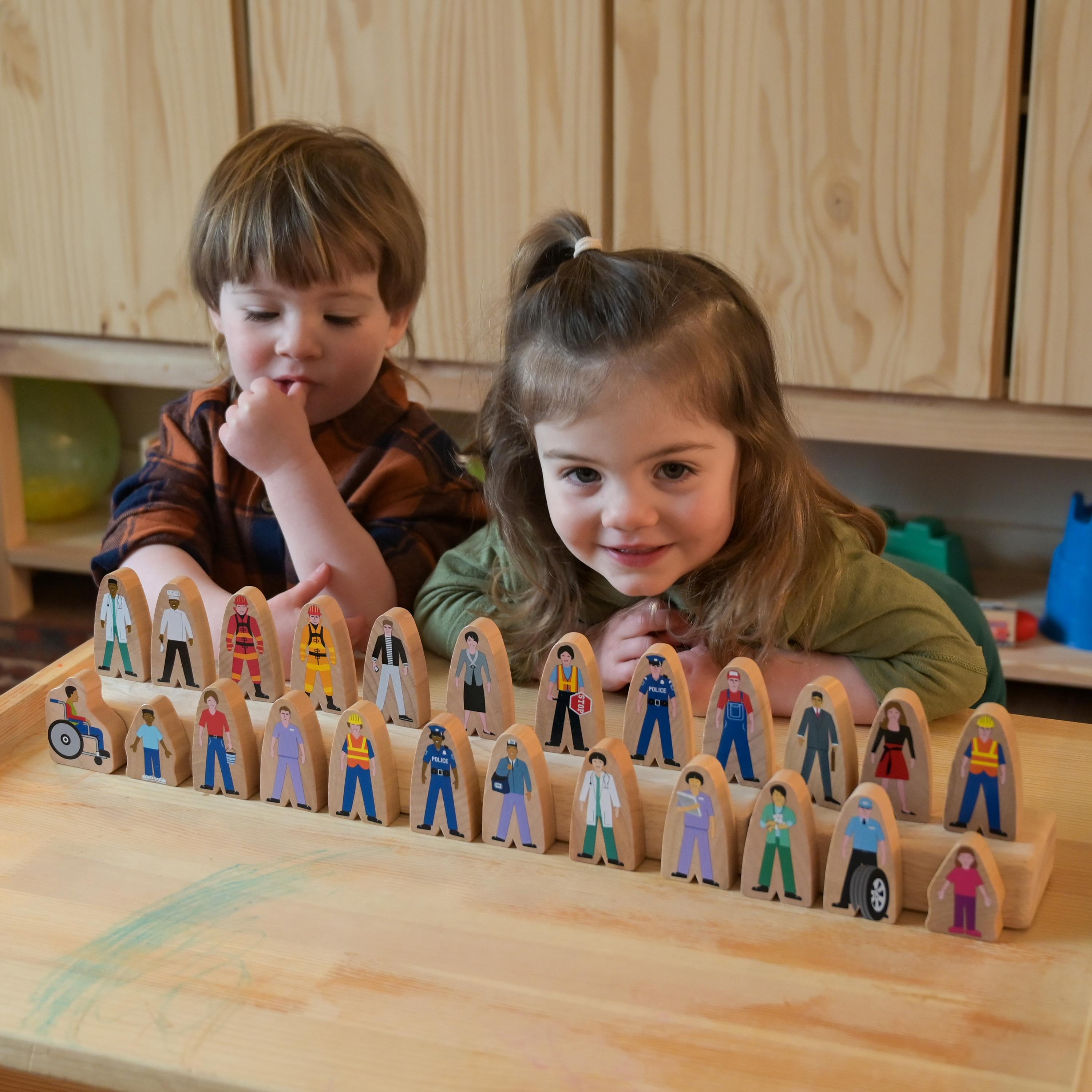 Two children playing with a set of wooden figurines on a wooden surface.