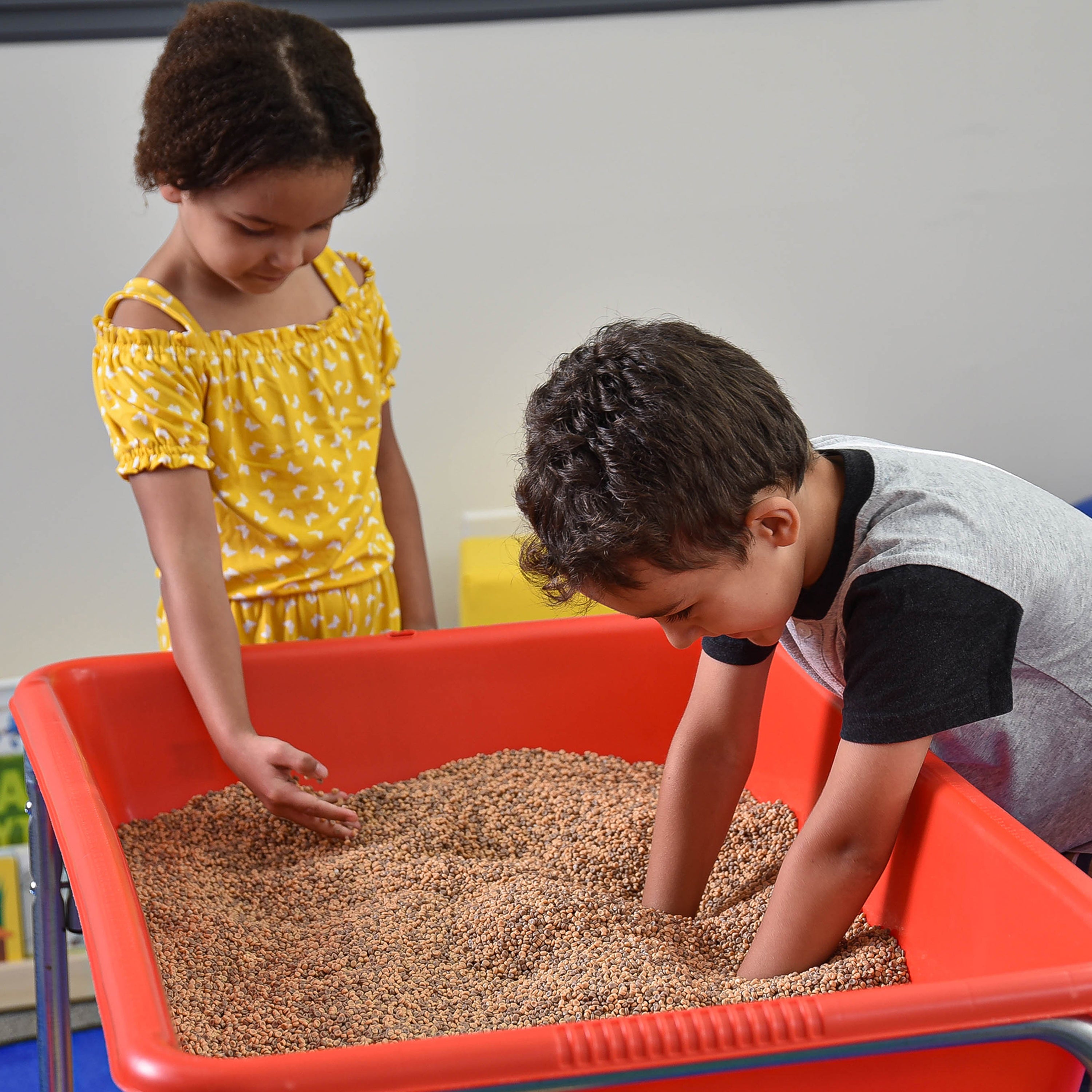 Two children playing with sand in a red bin.