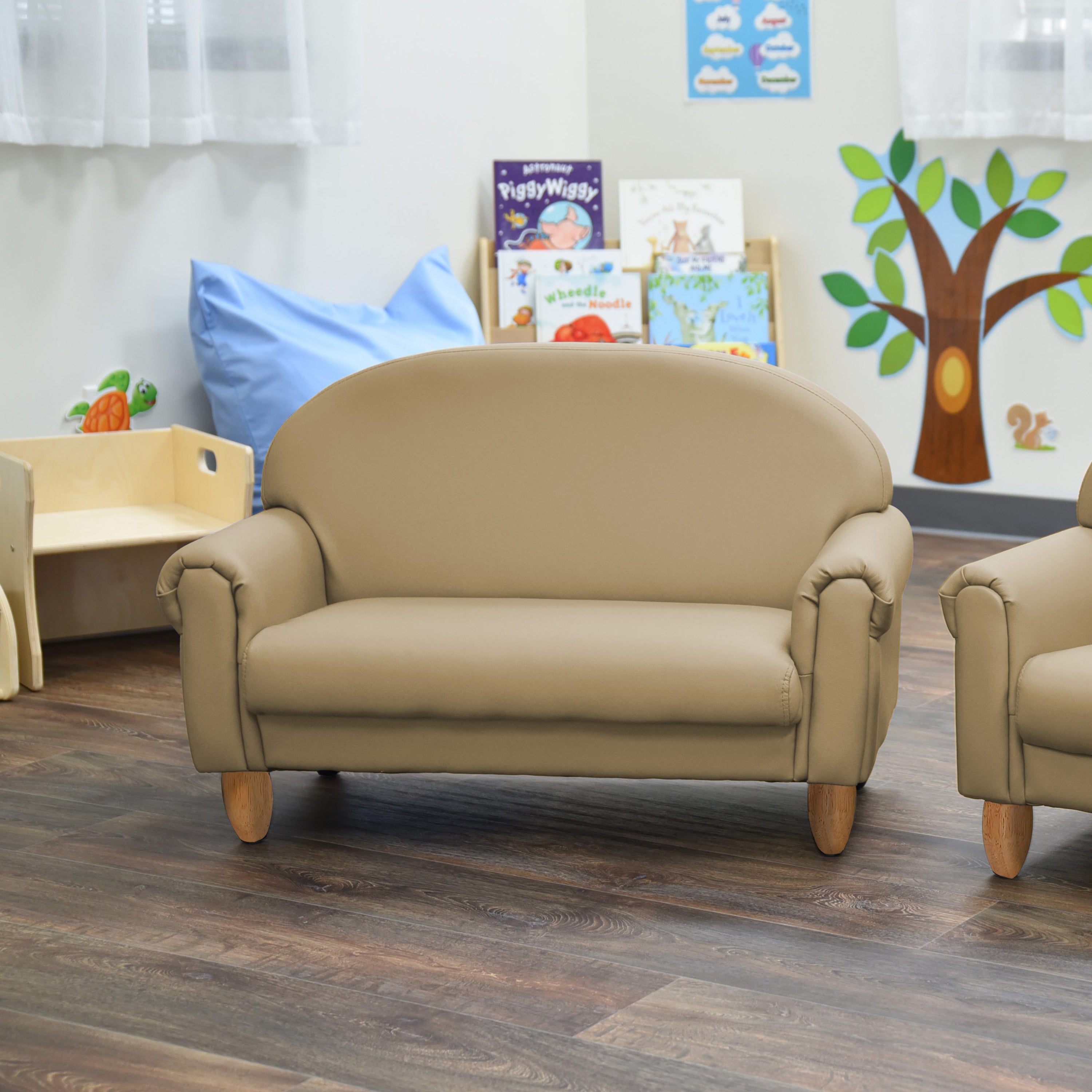 Beige children's sofa in a classroom setting with books and educational posters on a shelf.