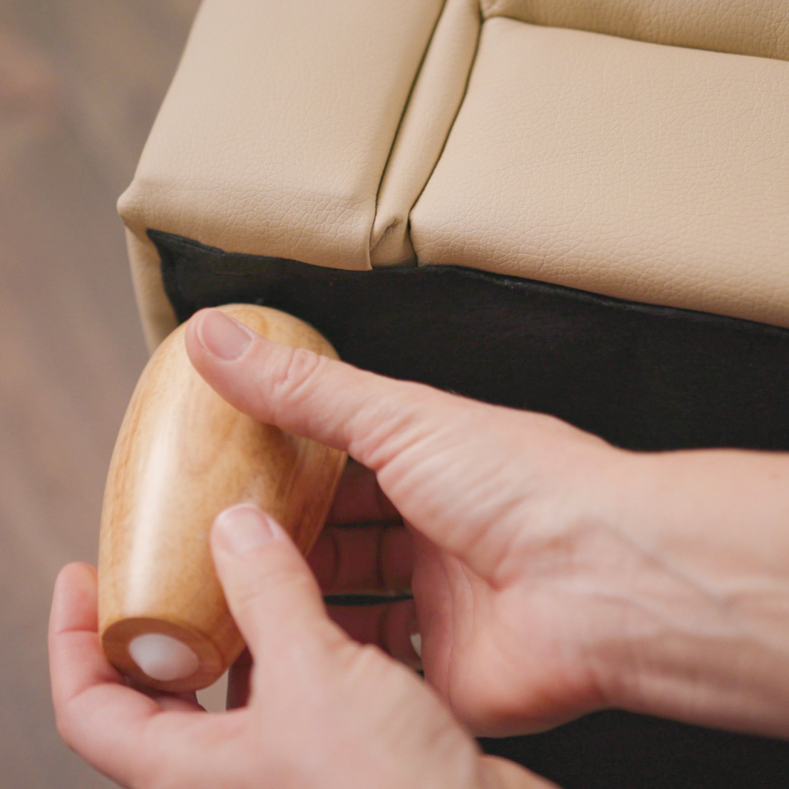 Close-up of a hand holding a wooden chair leg against a beige leather sofa