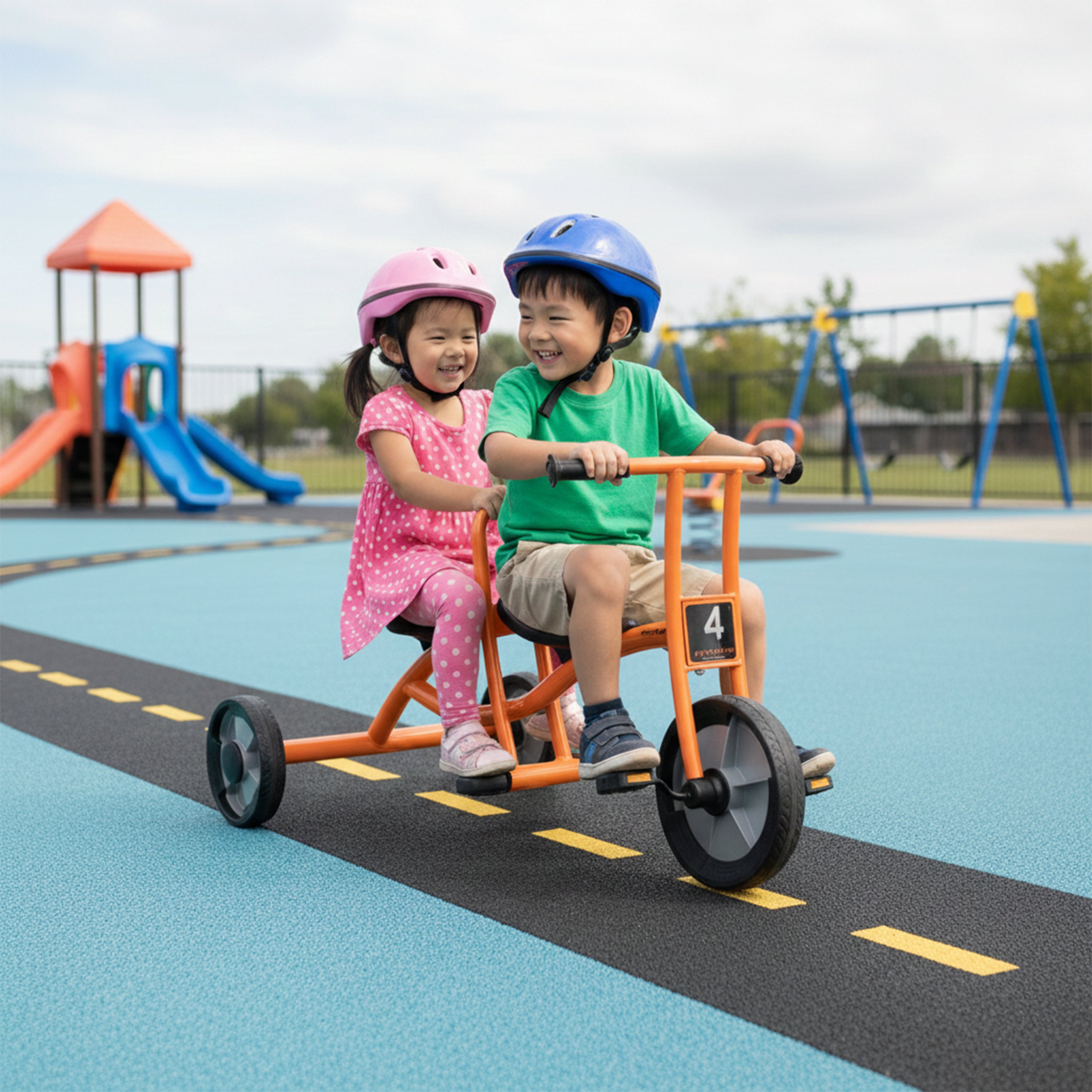 Two children riding a tandem bike on a playground with colorful equipment in the background.