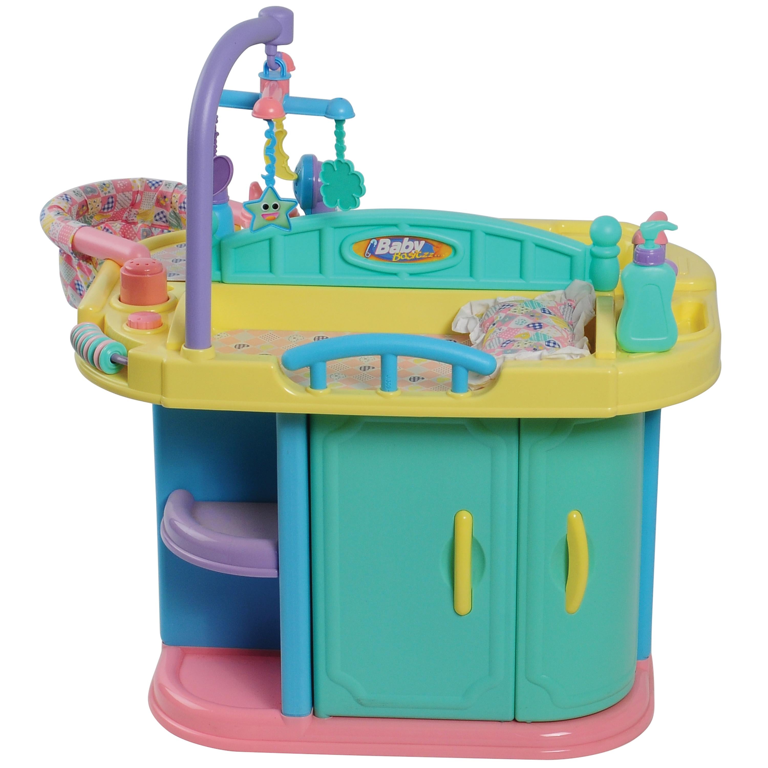 Baby playcaring toy playstation with turquoise, yellow, blue, pink, and purple plastic components, featuring a bassinet, mobile, changing tray, and storage cabinet on a white background.