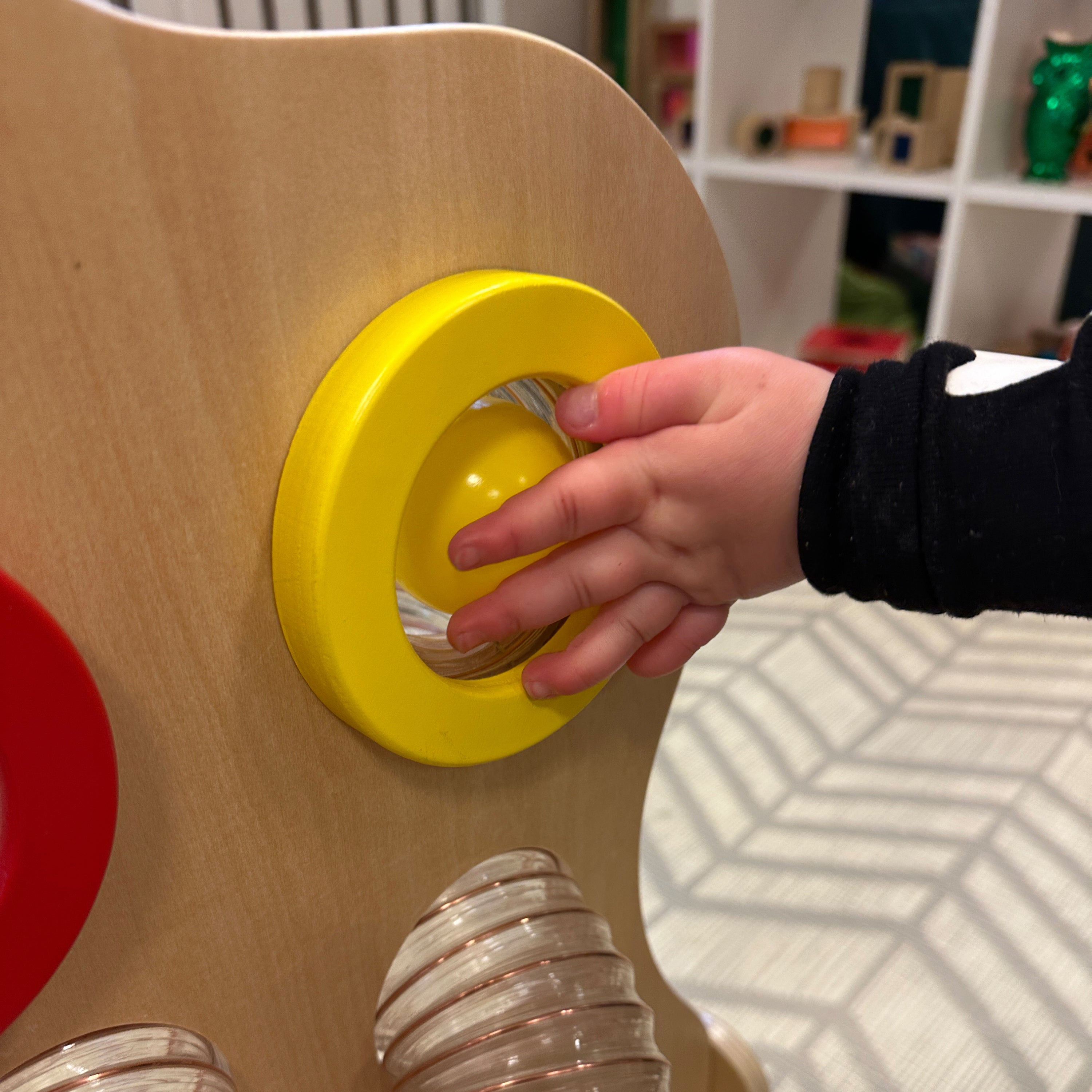 Child's hand interacting with a yellow button on a wooden toy structure.