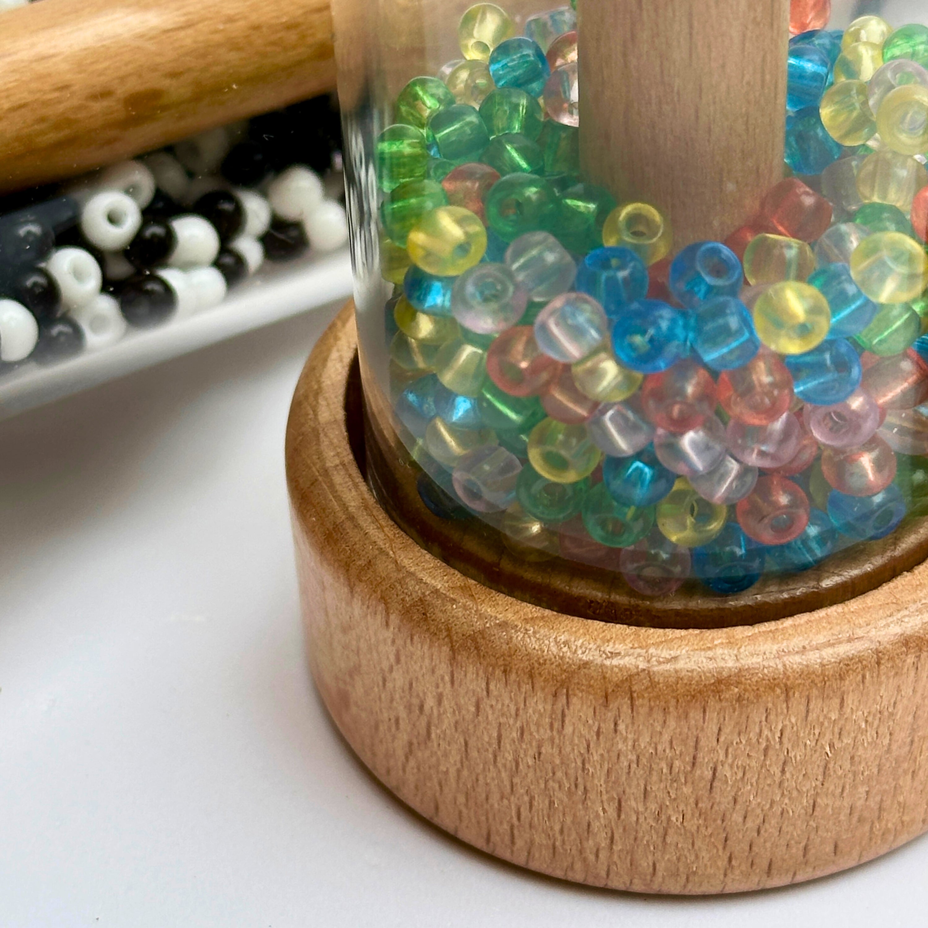 Colorful beads in a wooden container on a white surface