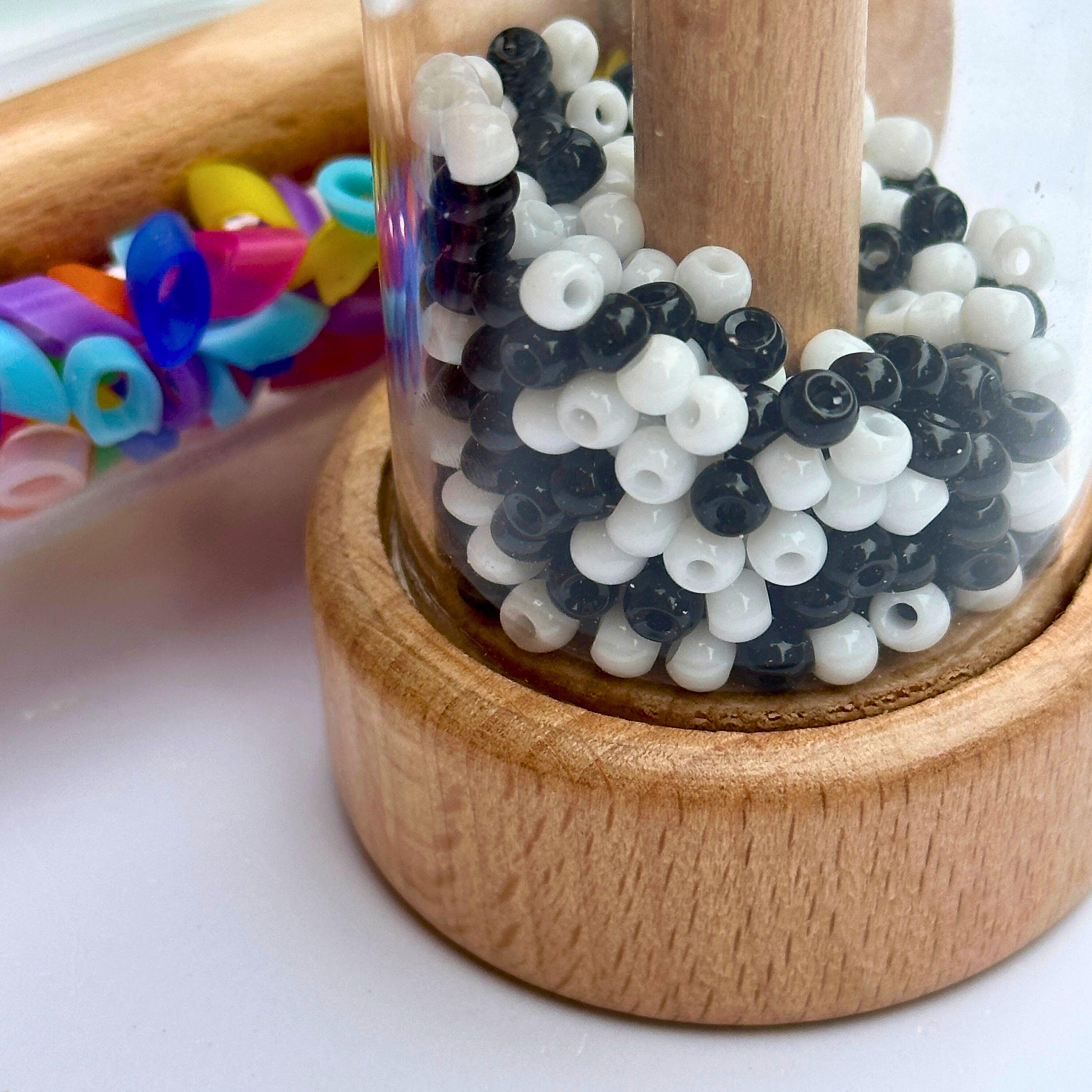 Plastic tube filled with black and white beads on a wooden base, with colorful beads in the background.