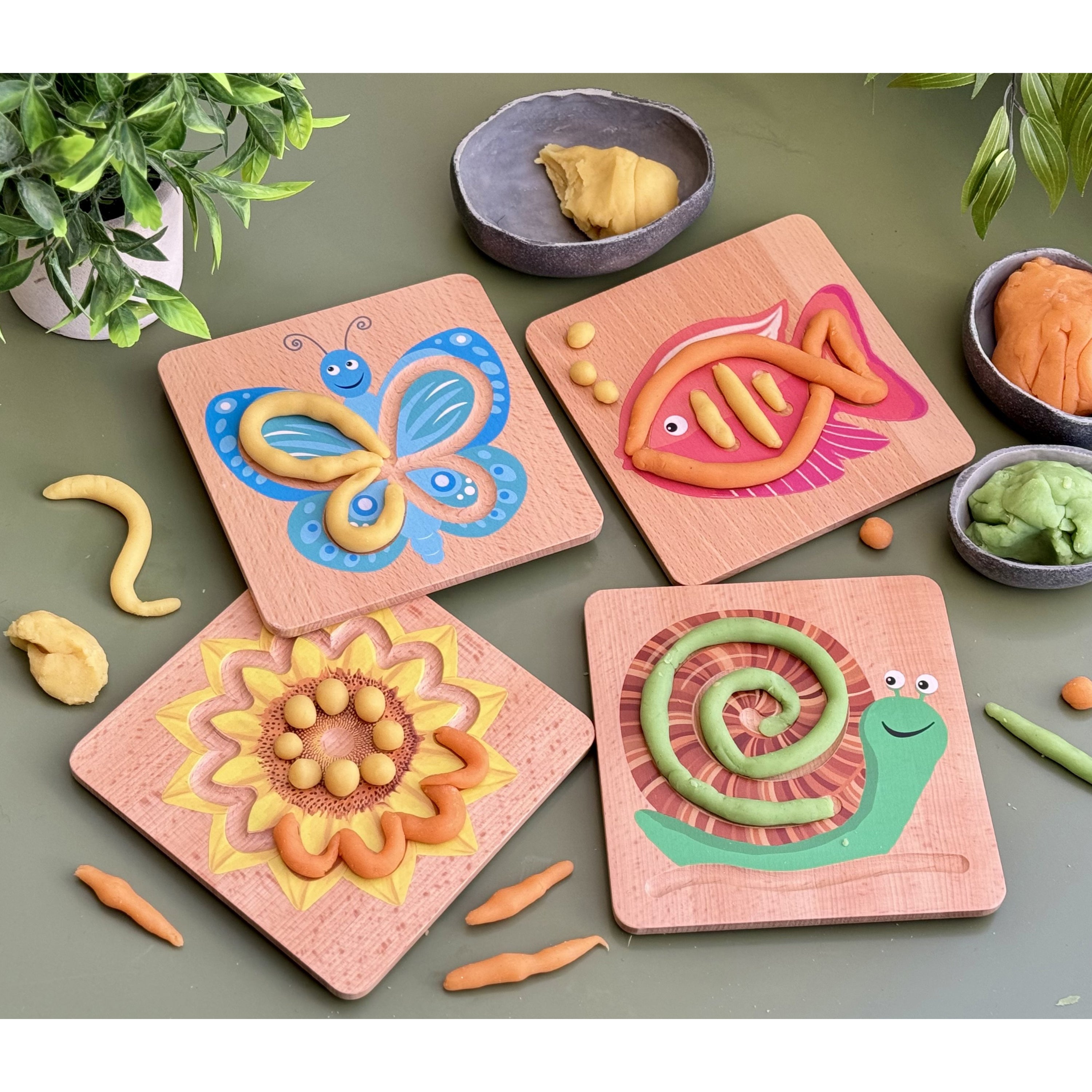 Colorful animal-shaped play dough on pink boards with small bowls of additional play dough on a green surface.