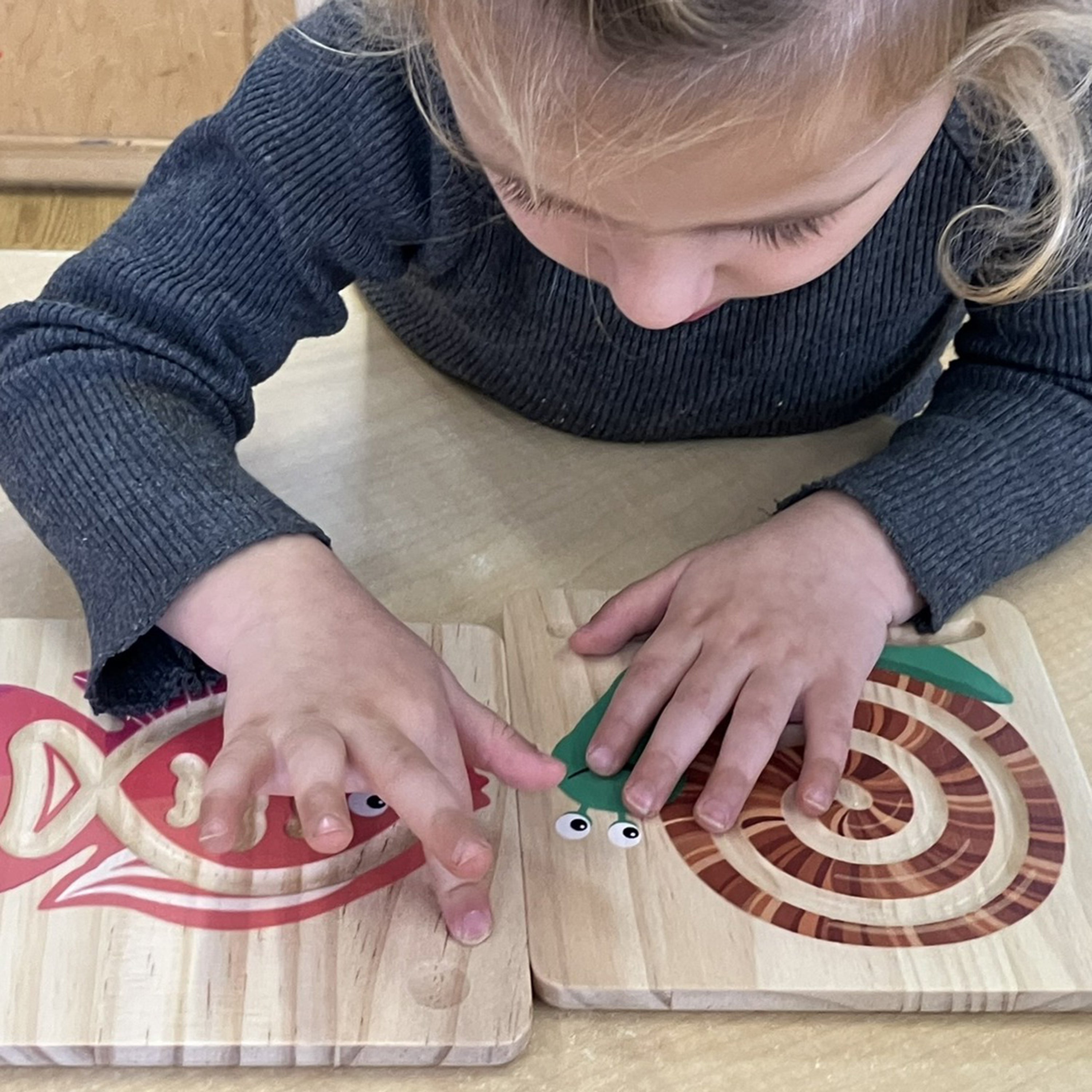 Child playing with wooden puzzle pieces on a wooden surface