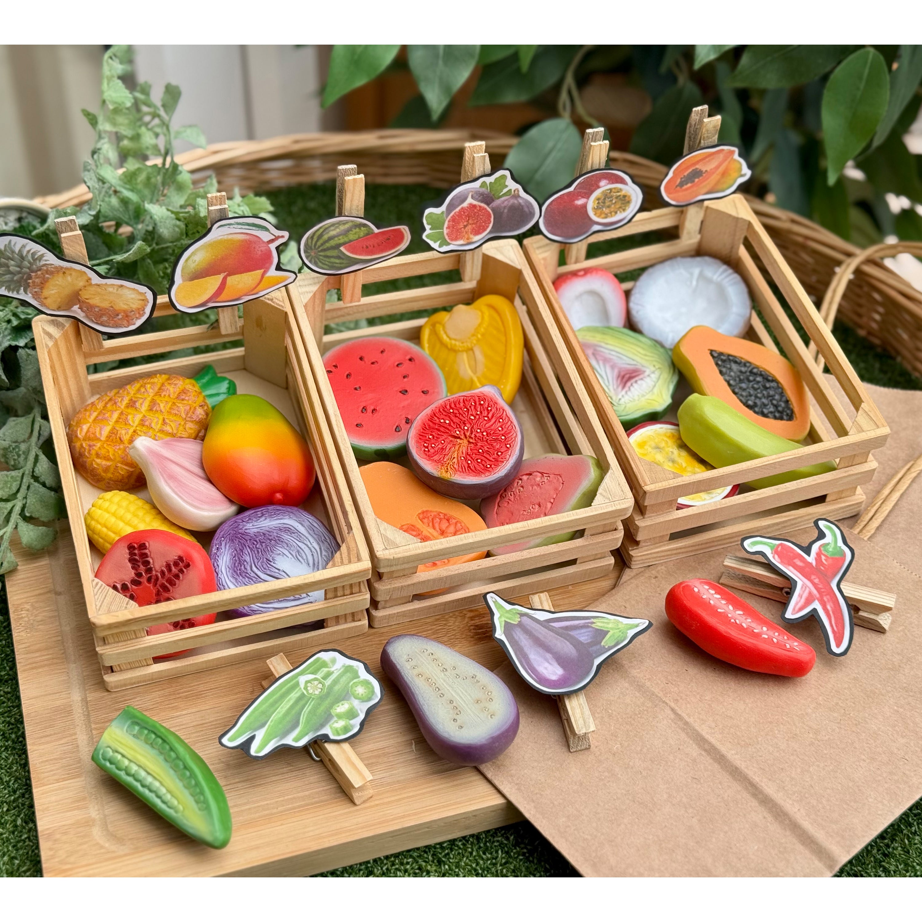 Wooden toy fruit and vegetable set in a crate with greenery in the background