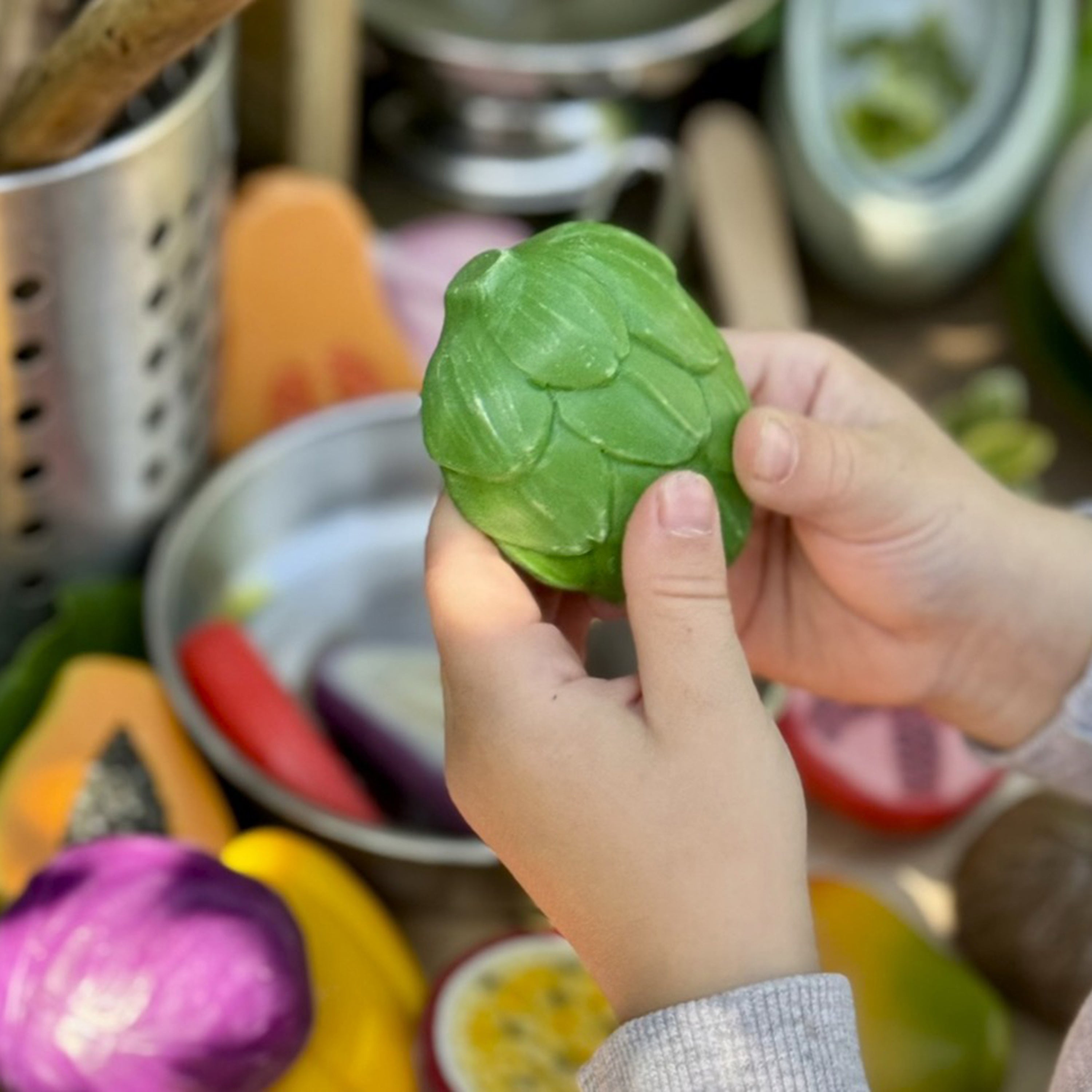 Hand holding a green leafy vegetable with kitchen utensils in the background