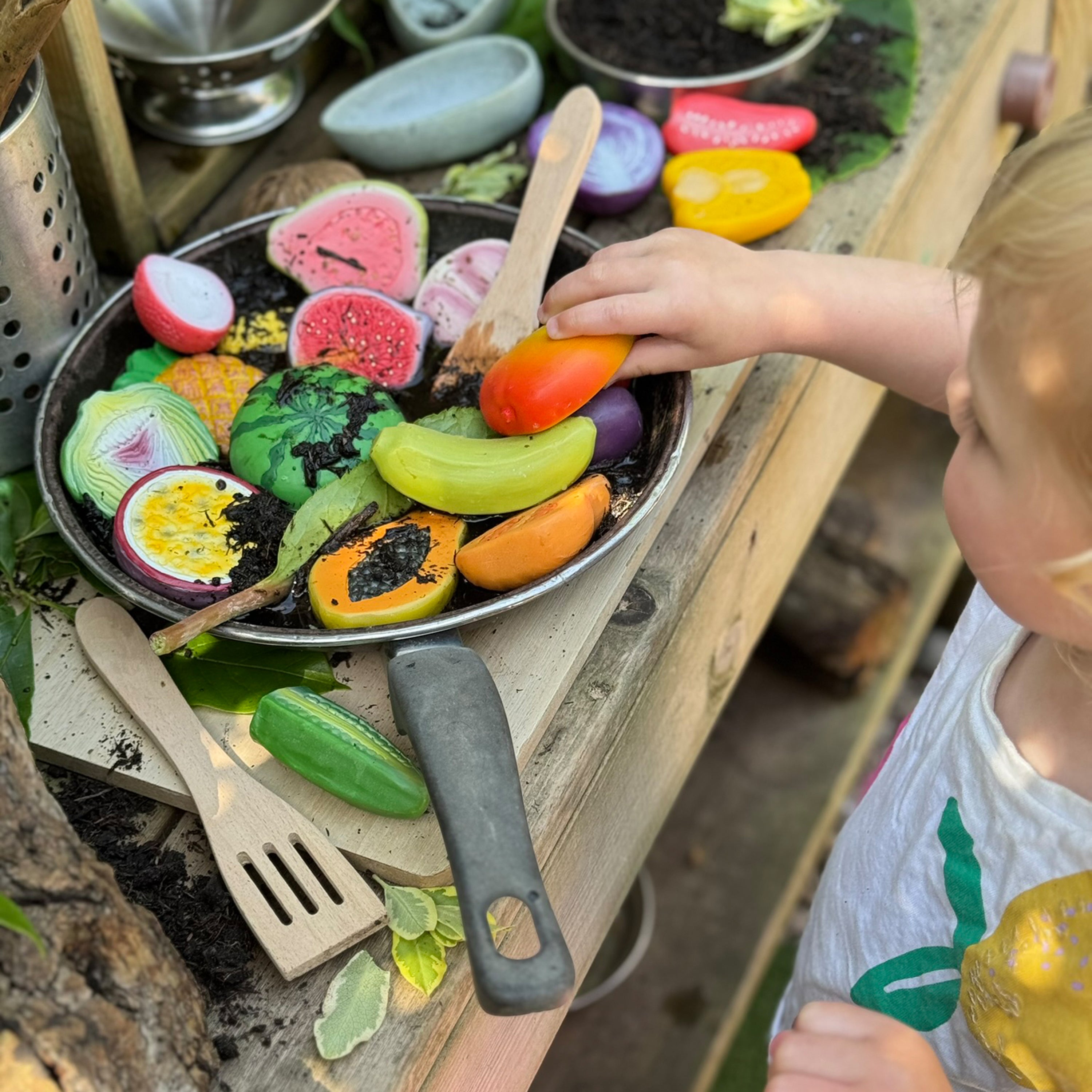 Child playing with toy vegetables and fruits in a pan outdoors