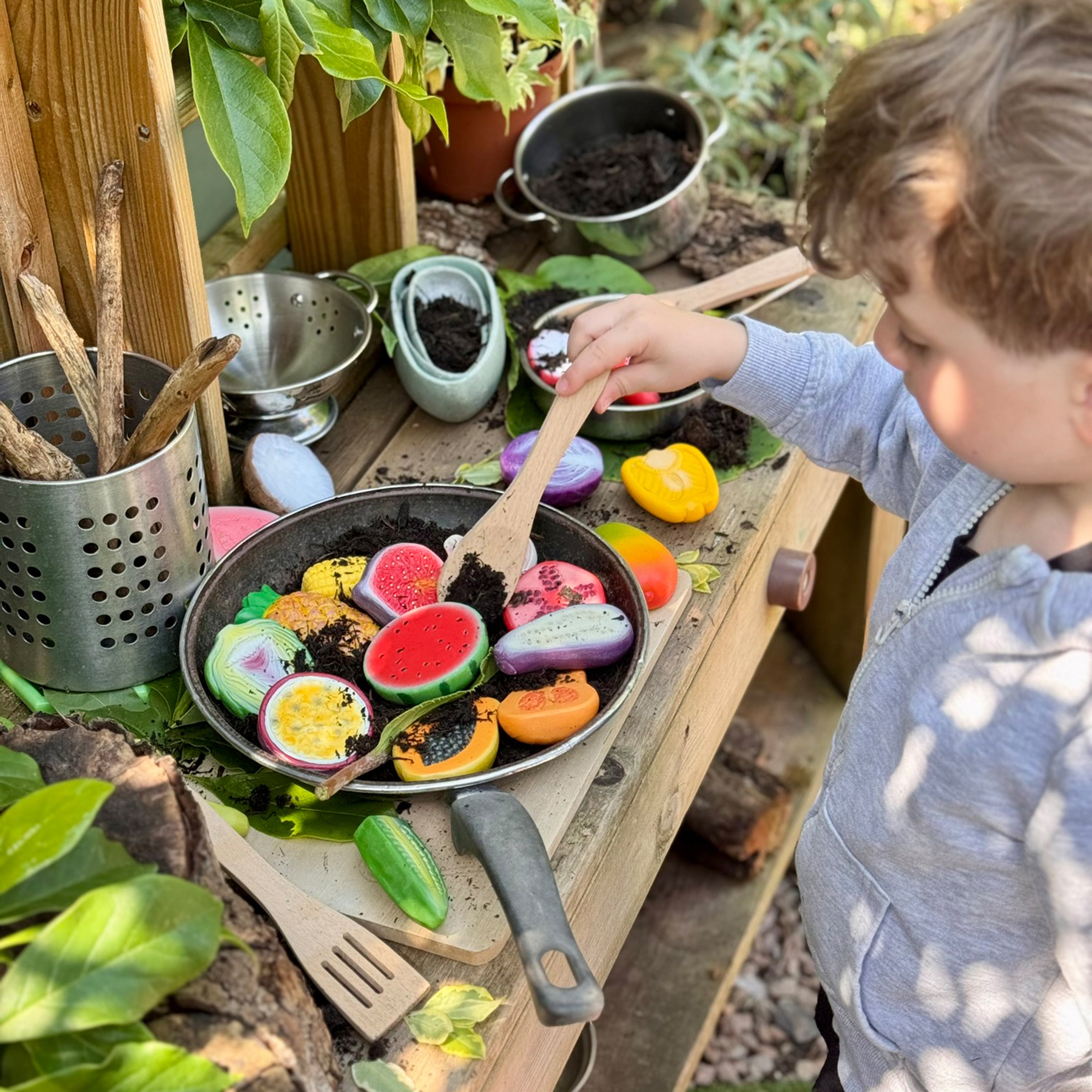 Child playing with toy fruits and vegetables in a pan outdoors