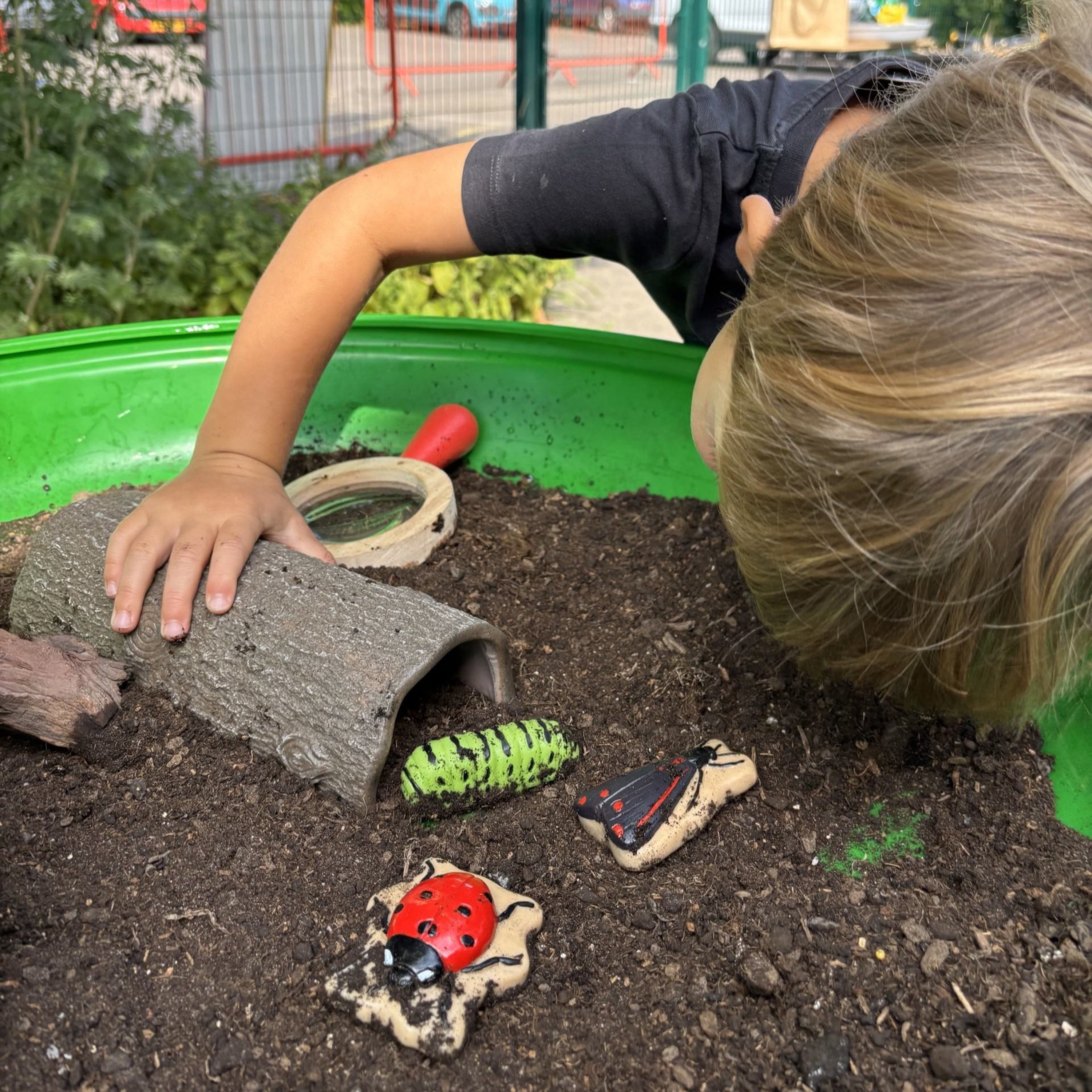 Child playing with toy insects and a tunnel in a sand pit outdoors