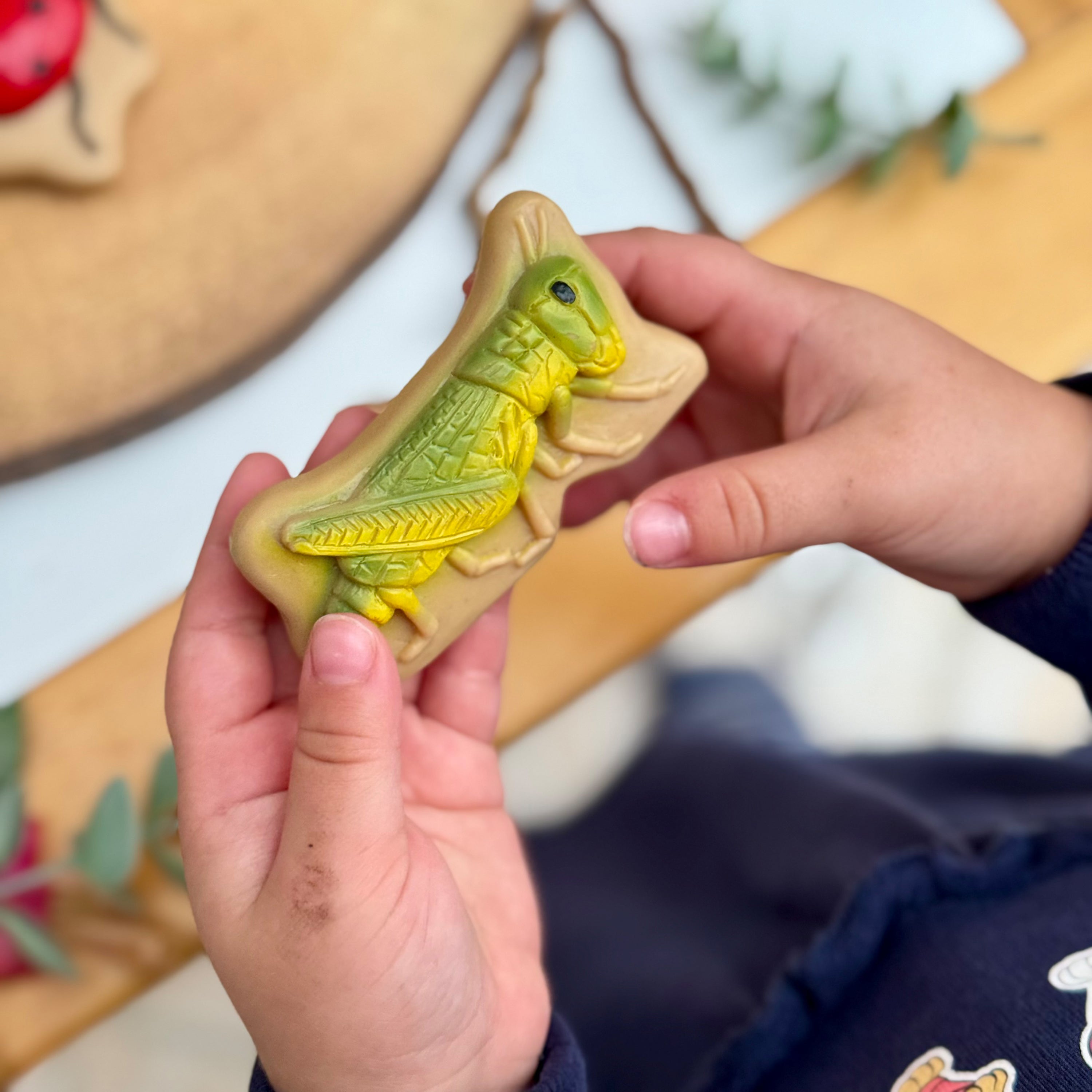 Hand holding a yellow and green grasshopper-shaped stone