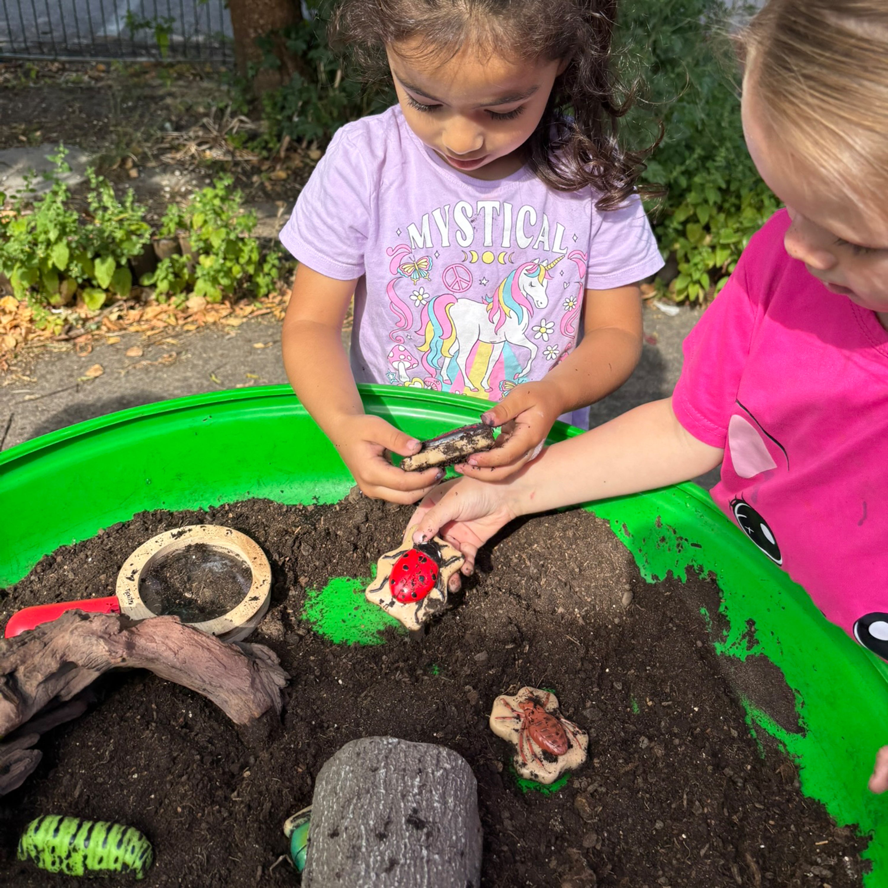 Two children playing with a small garden or terrarium on a green tray.