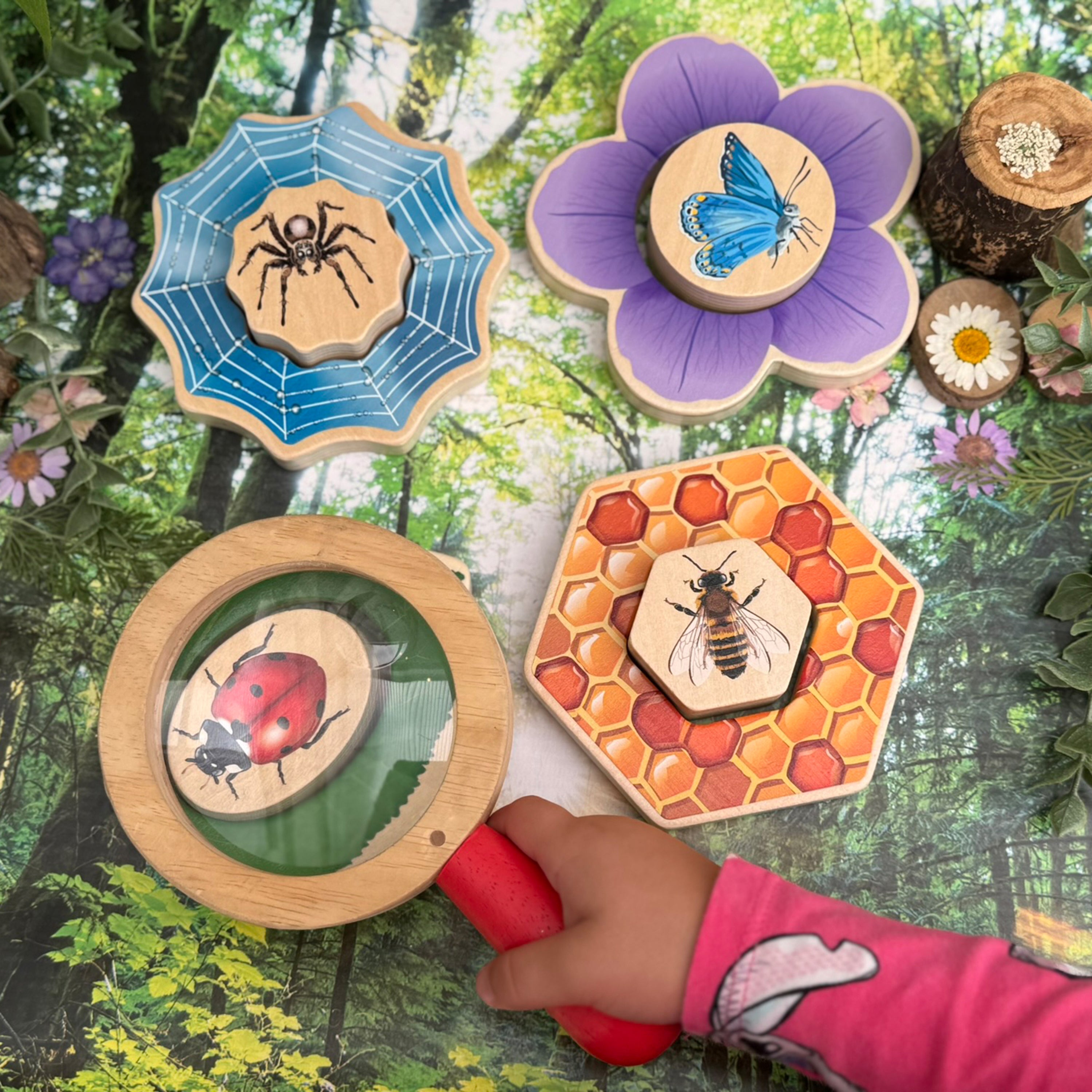 Wooden educational toys shaped like a spider, flower, ladybug, and honeycomb held by a child against a forest background.