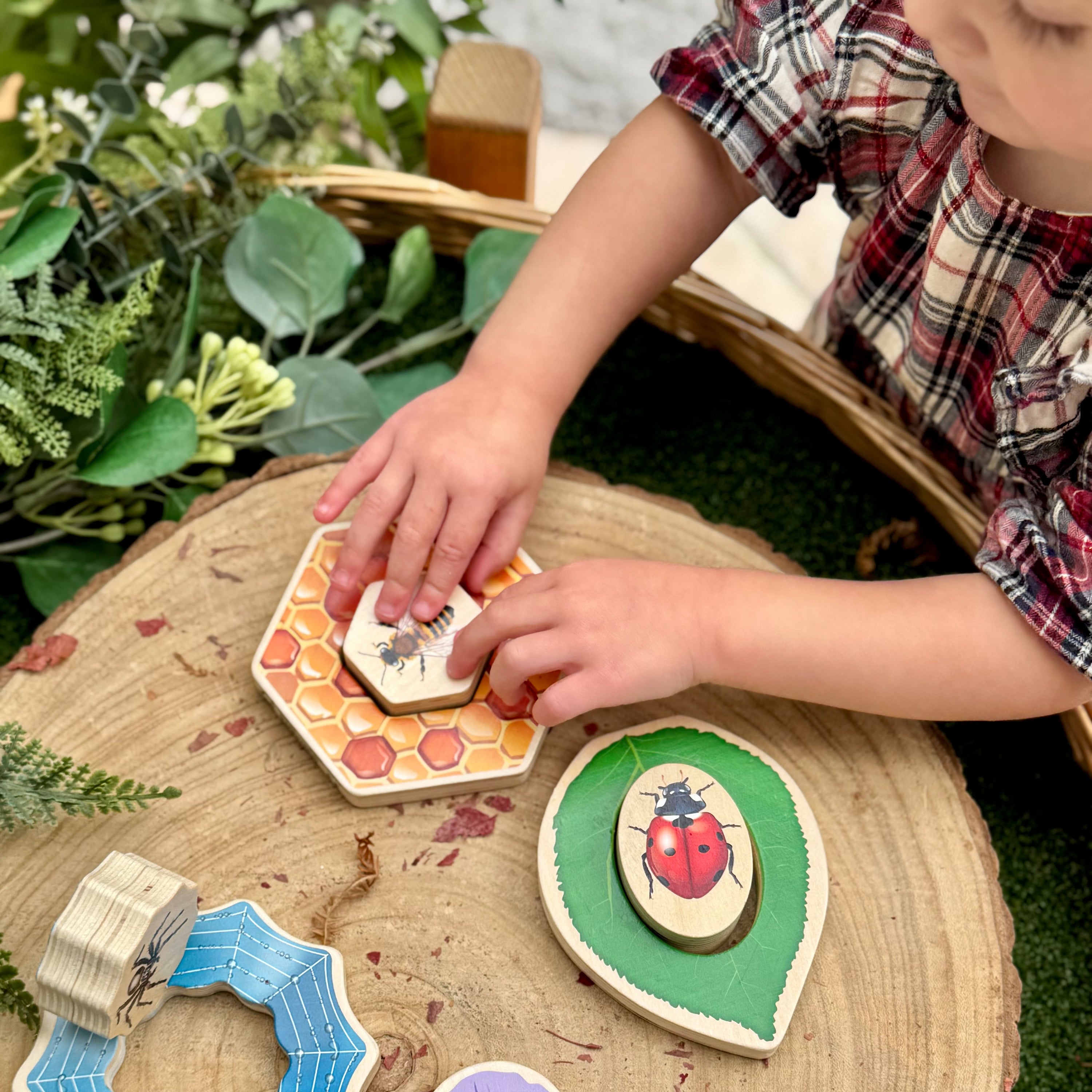 Child playing with wooden insect toys on a natural surface with plants in the background