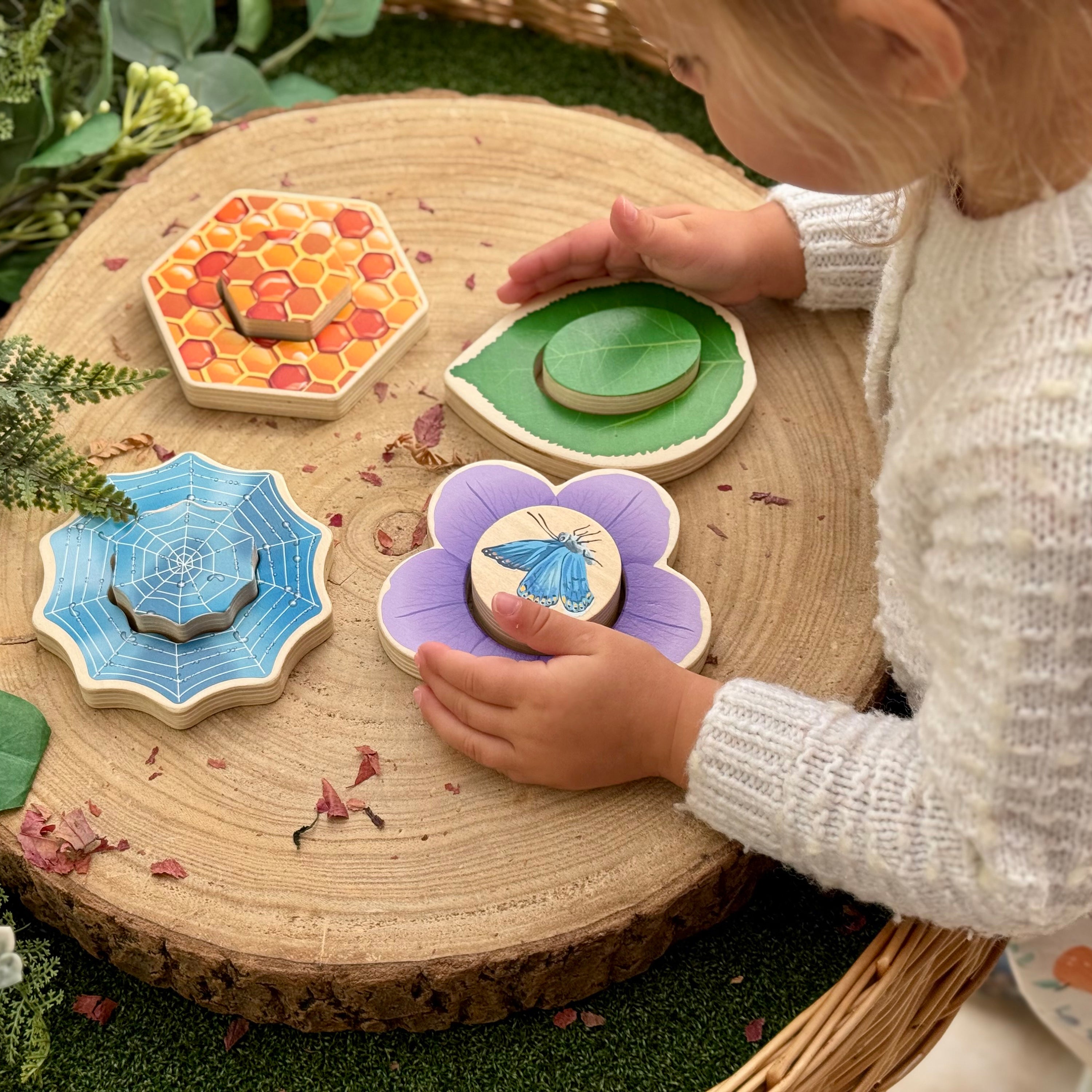 Child playing with wooden nature-themed tiles on a wooden surface