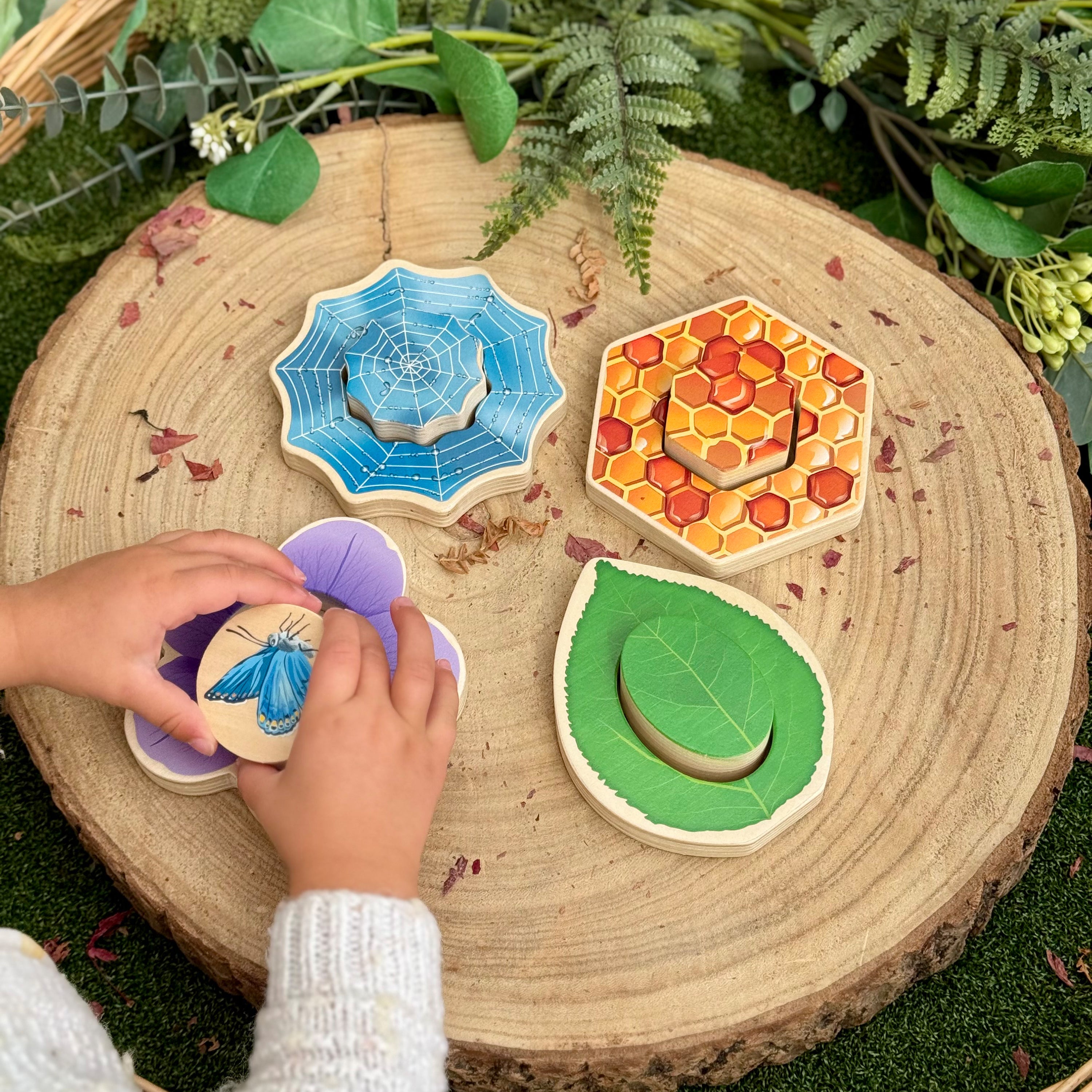 Child playing with wooden nature-themed toys on a wooden surface with greenery.