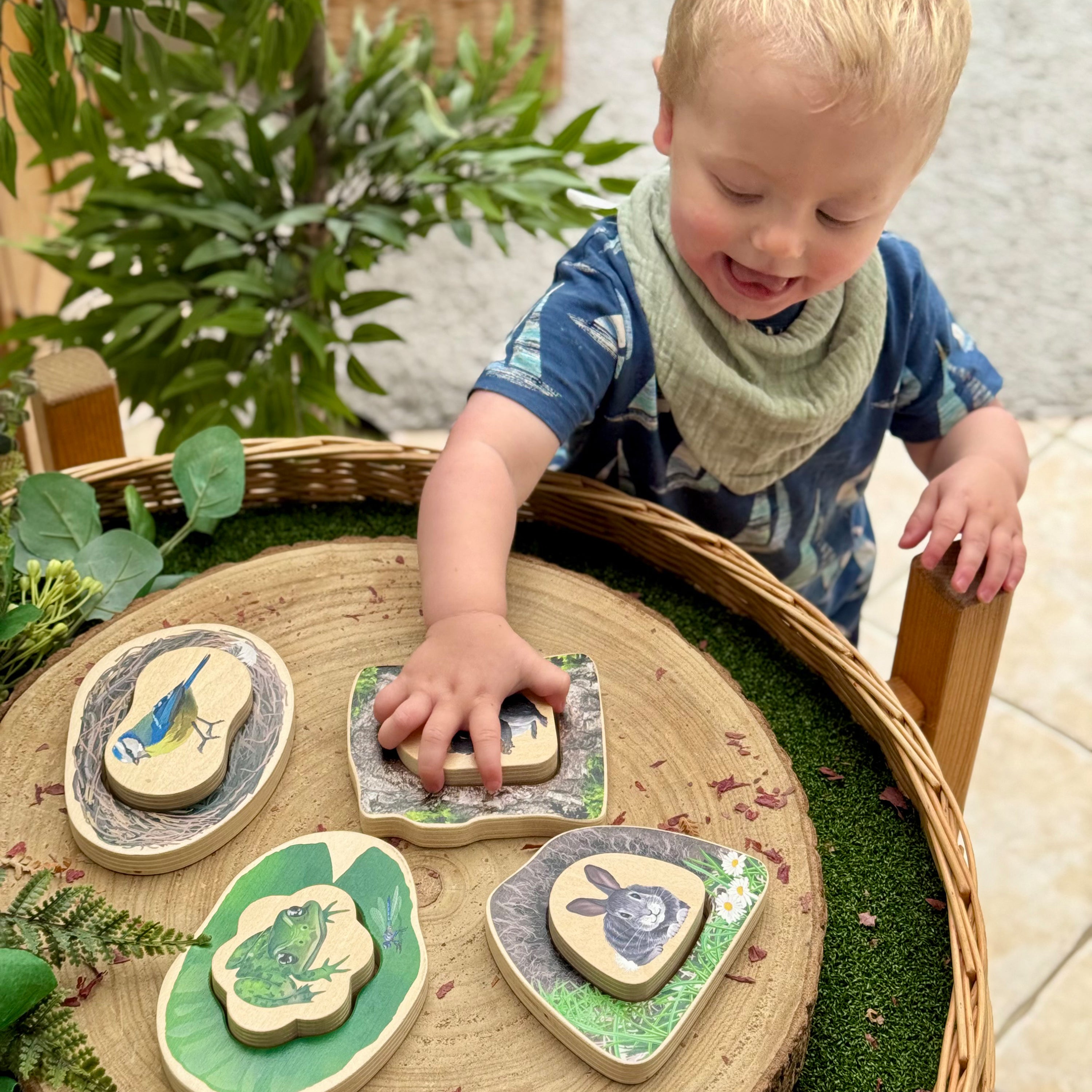 Child playing with nature-themed wooden stones on a woven tray outdoors.