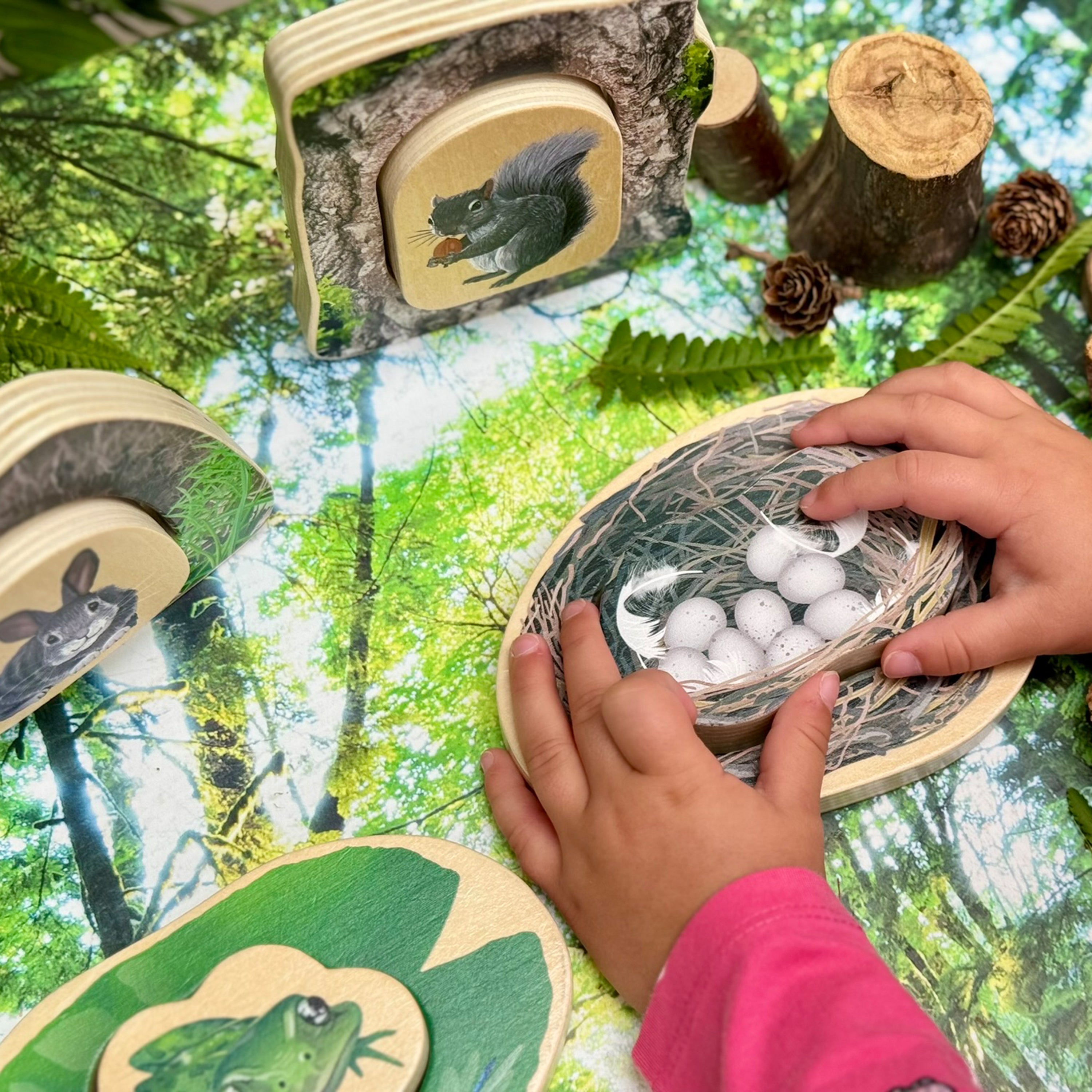 Children's hands interacting with a wooden nature-themed puzzle set against a forest background.